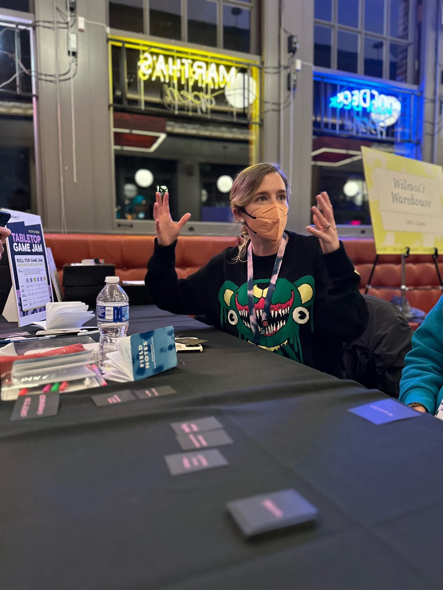 Person with blonde hair and a scary sweater gesturing while playing cards