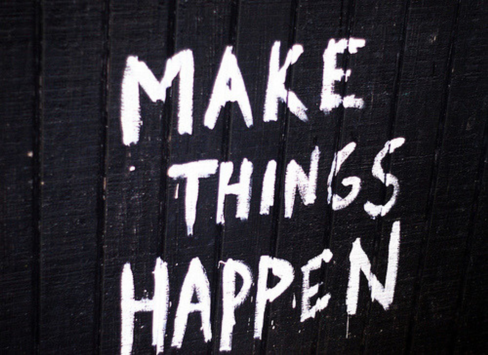 sur un mur de planches peint en noir, des lettres peintes en blanc "Make things happen"