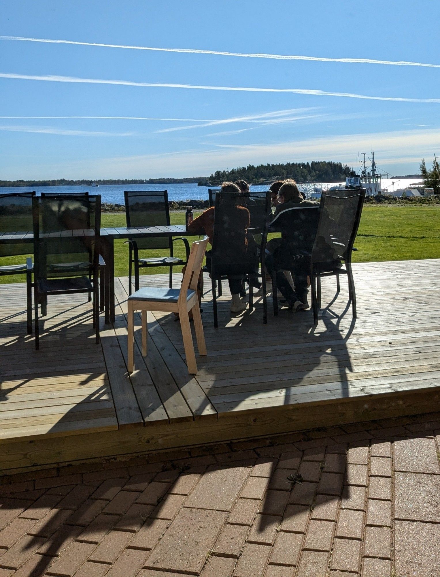 Group of people sitting on a terrace studying papers, with blue sky and blue sea behind