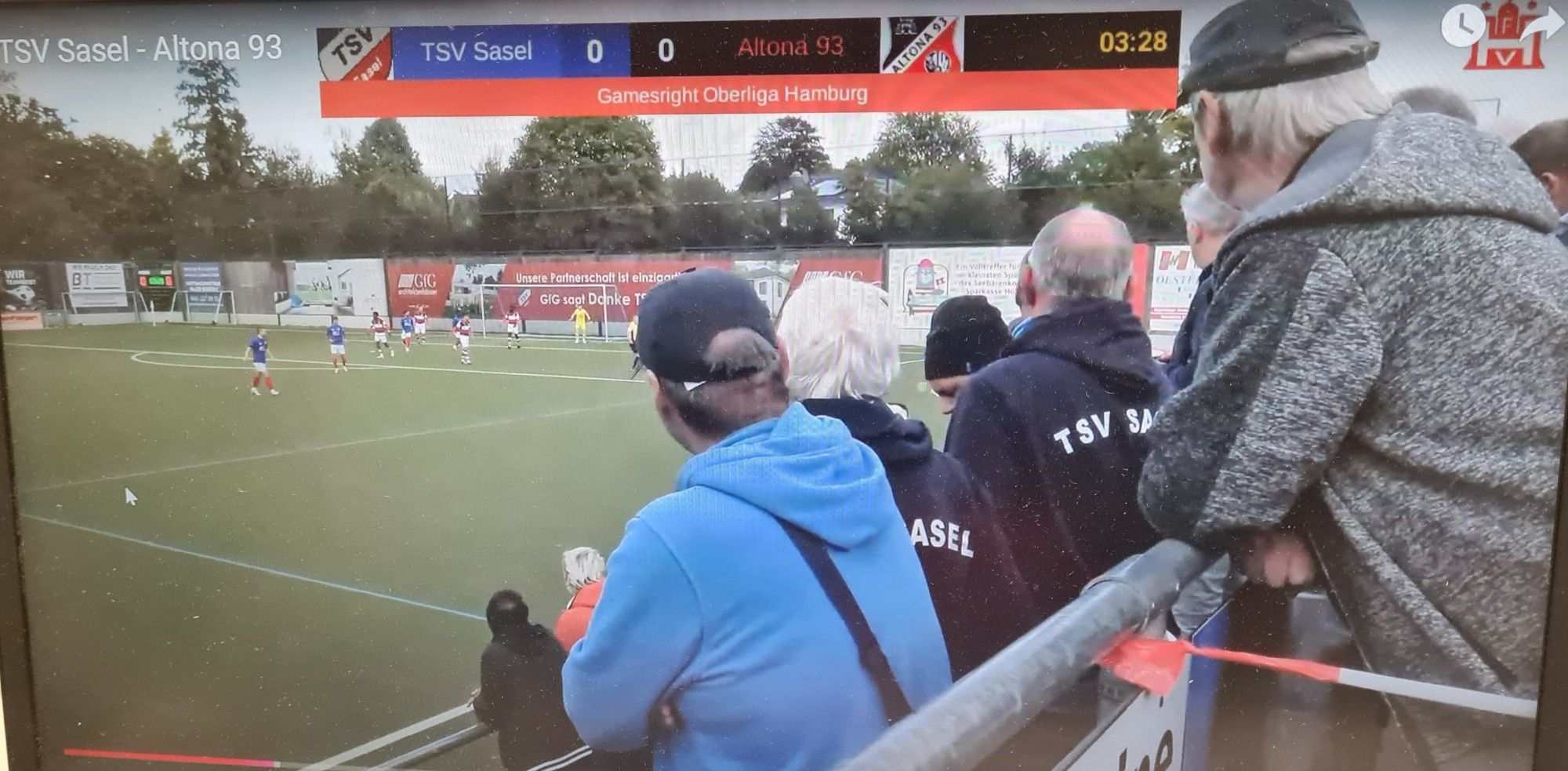 Standbild Stream Sasel - Altona. Die Hälfte des Spielgeschehens inkl. ballführendem Spieler wird durch Zuschauer verdeckt.