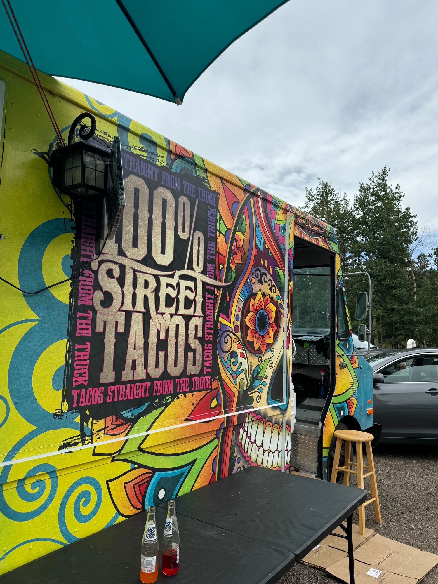 Photo of a food truck that says “100 percent Street Tacos” with two glass bottled Fanta soda on a table in the foreground 