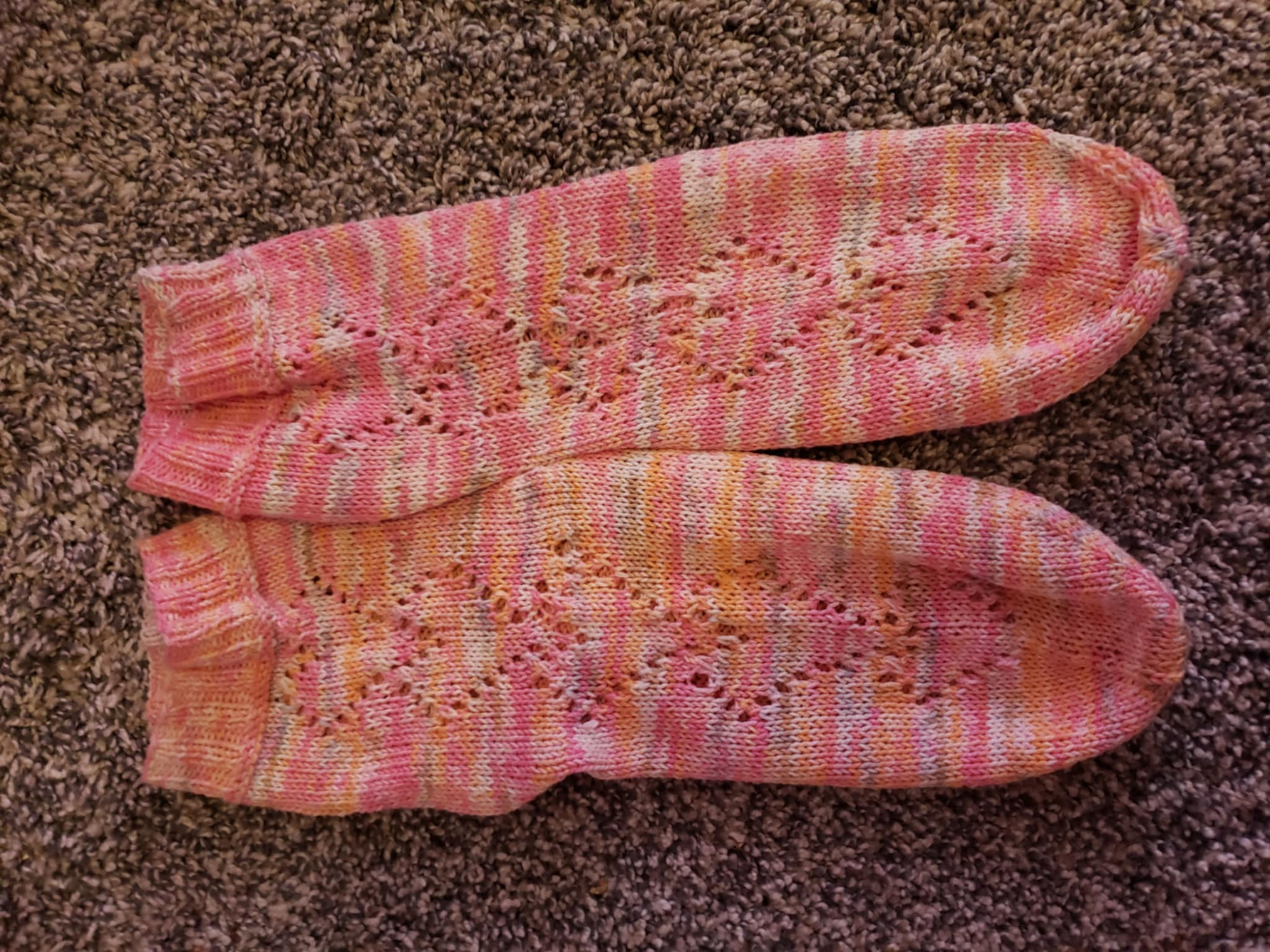 A pair of socks in the lesbian pride colors laid flat on the floor. They have a repeating heart lace motif.