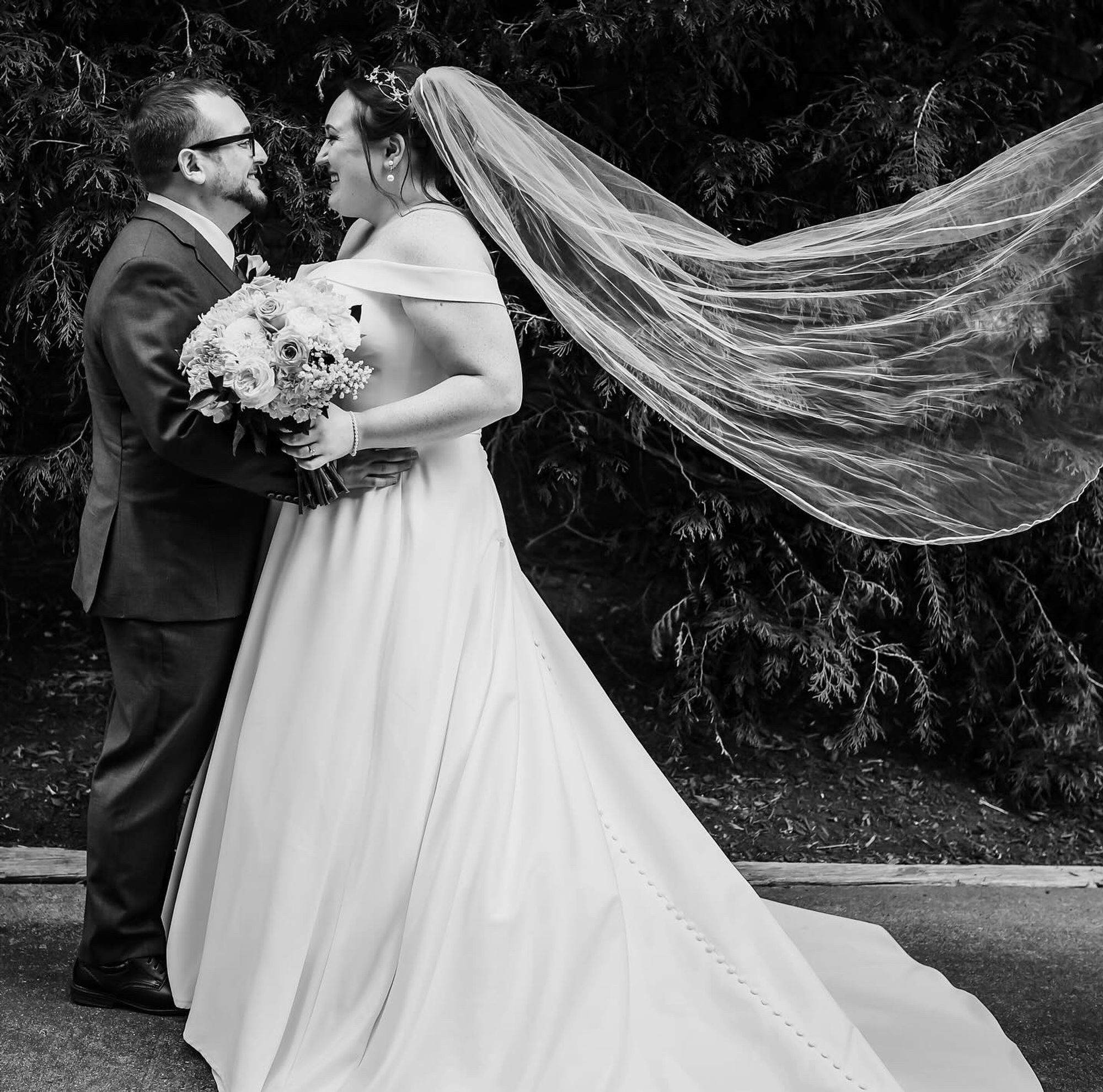 A bride and groom, with the bride’s veil blowing in the wind