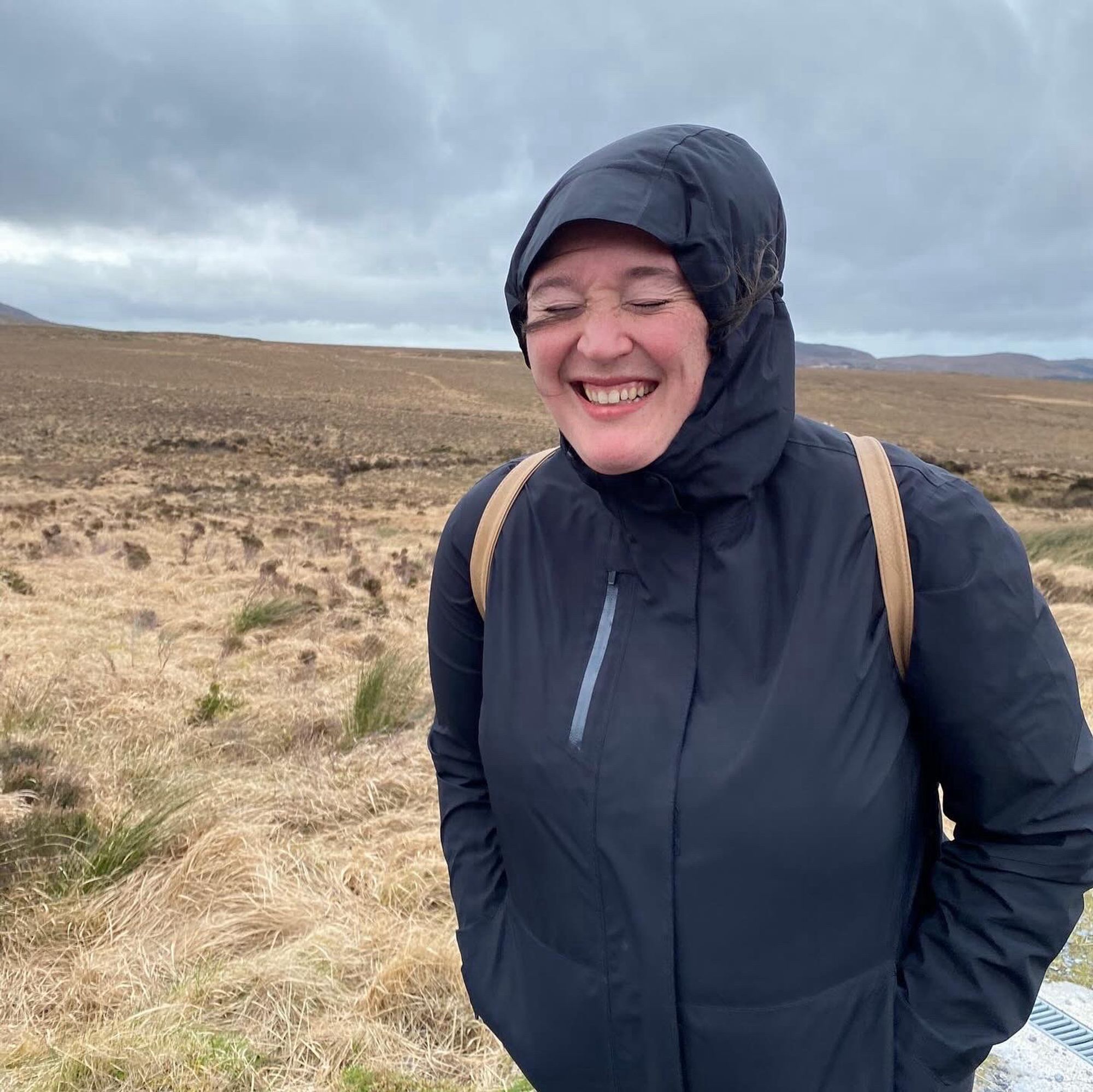 A woman in a black rain jacket struggles against the wind