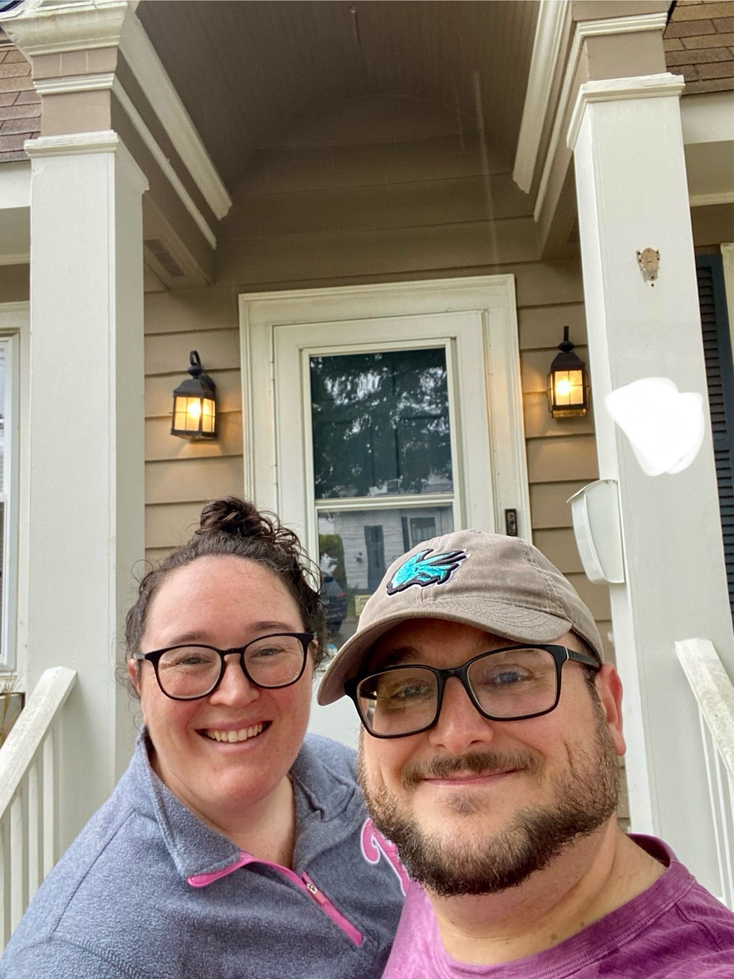 A man and woman with glasses smile on a front stoop