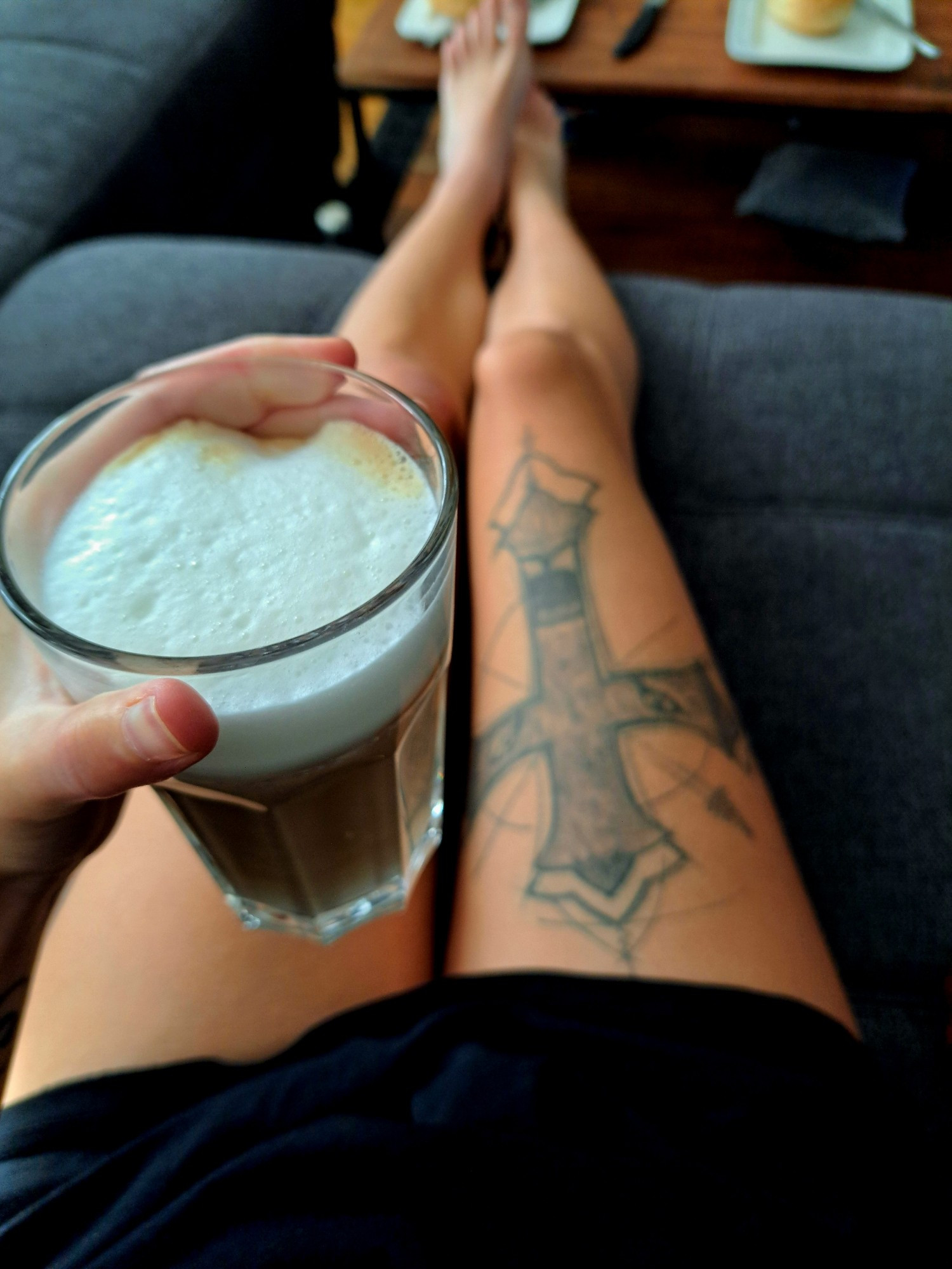 Lecki schmecki Latte macchiato in der Hand und nackte Beine ausgestreckt auf dem Sofa etwas unscharf im Hintergrund