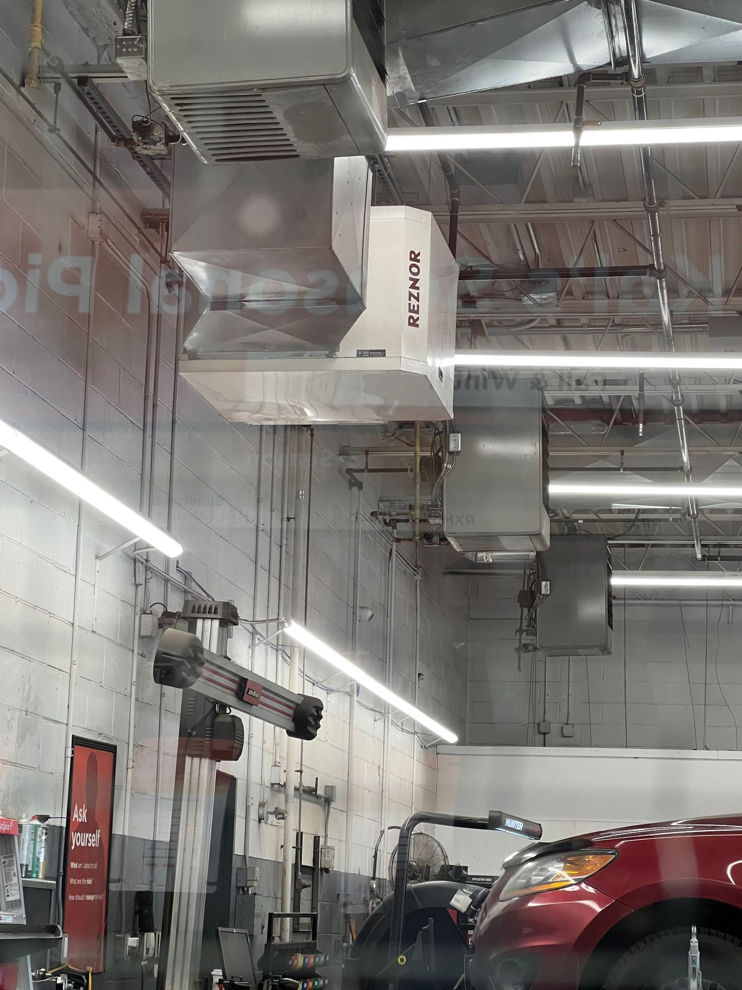 A view of the interior of an auto repair shop with cars on lifts and various bits of machinery. There’s a boxy HVAC system on the ceiling with one box labeled “REZNOR”