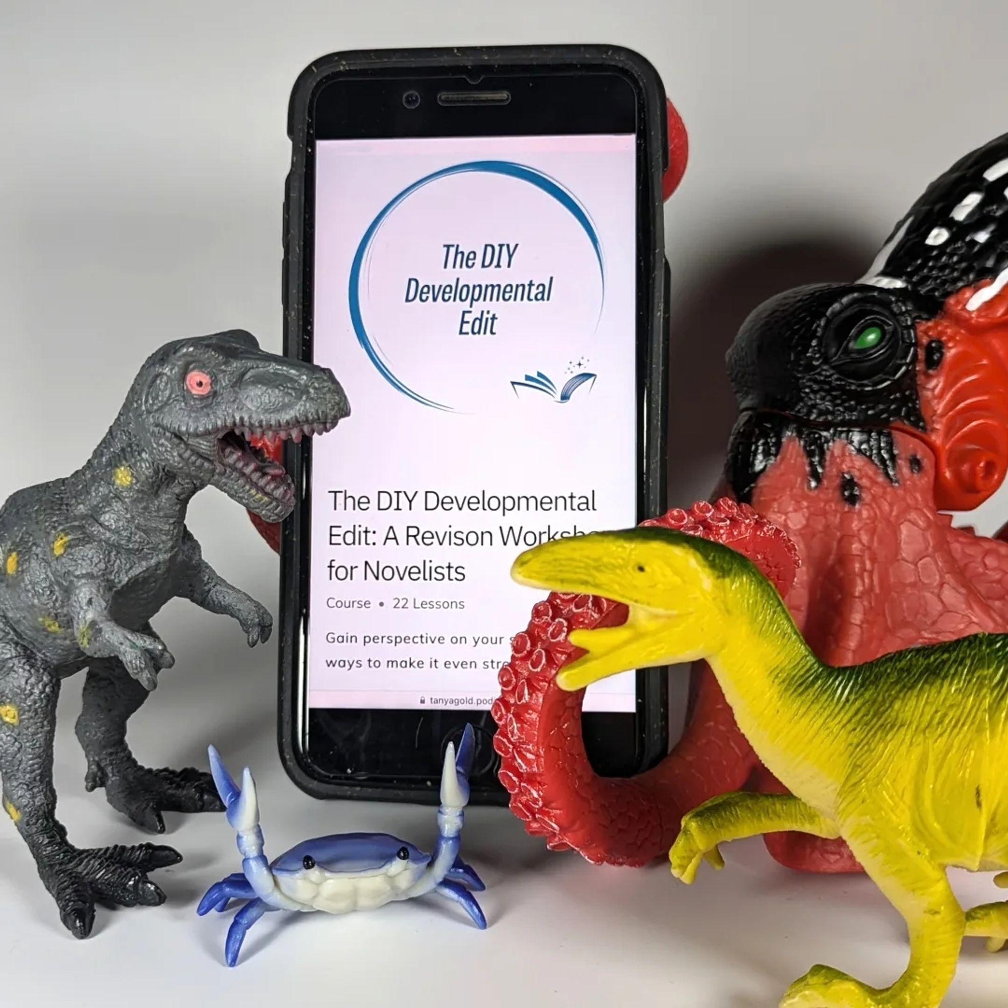 A toy octopus holding a phone with the DIY Developmental Edit course displayed on it. There are two toy dinosaurs and a crab surrounding them.