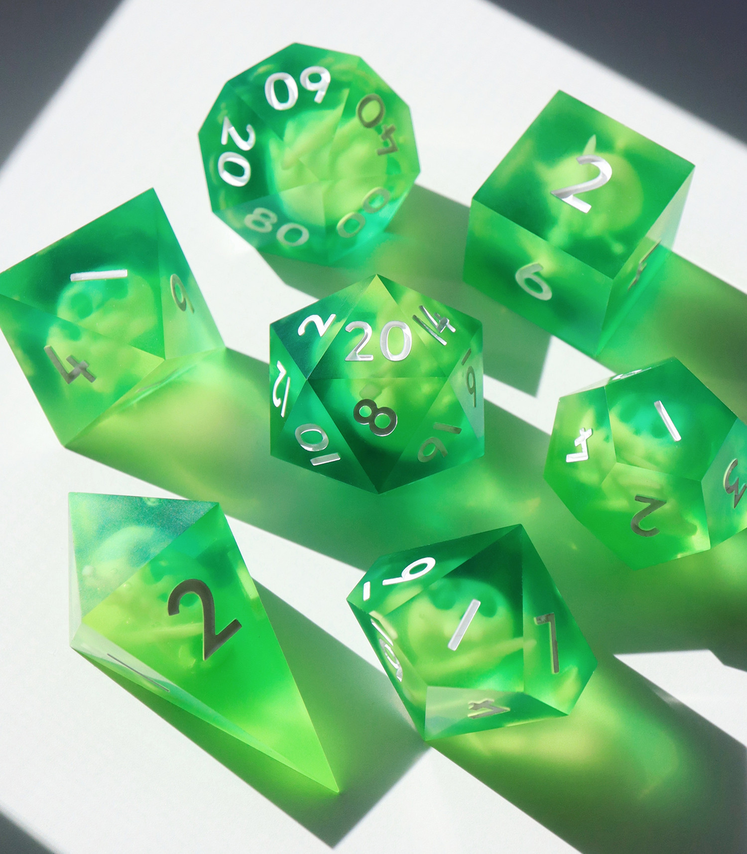 Full 7 piece set of Gelatinous Cube on a white background, all arranged in a circle with the D20 in the center. All the dice are oversized 40mm dice make of a semi-opaque bright green resin with floating inclusions of skulls and bones.