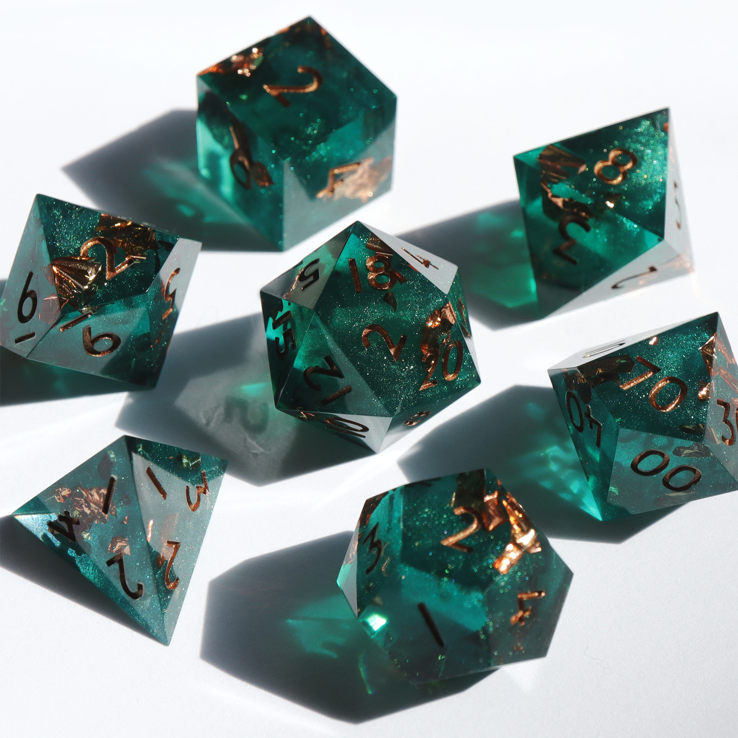 Full set of Decay Deco 7 piece dice set on a white background. All the dice are a semi-opaque teal with sparkles and gold foil. The numbers on the dice are gold.