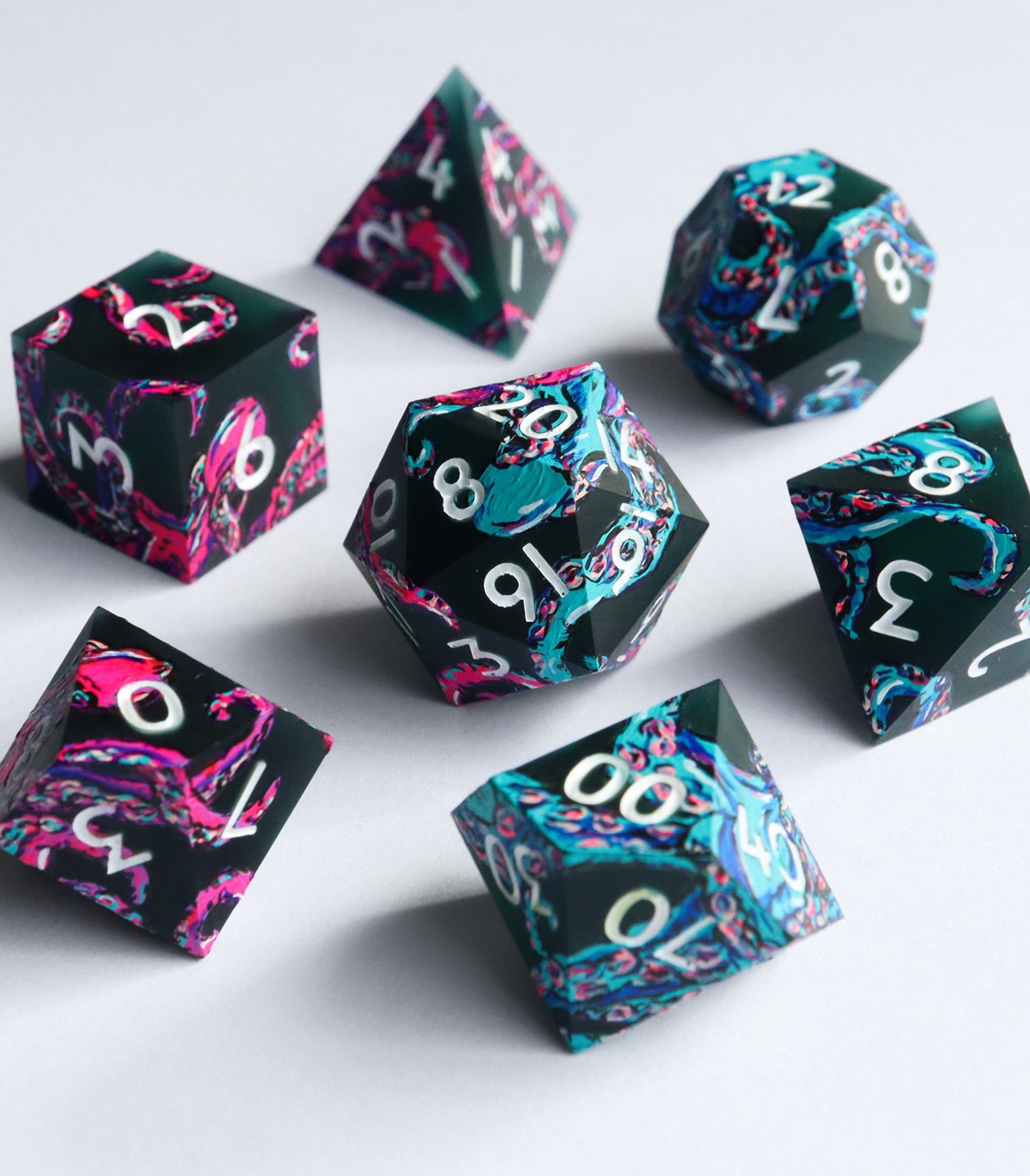 Full set of the con-exclusive Neon Abyss on a white background. The dice are a very dark matte green with hand-painted neon pink and blue octopi and tentacles on the surface. The numbers on the dice are white.