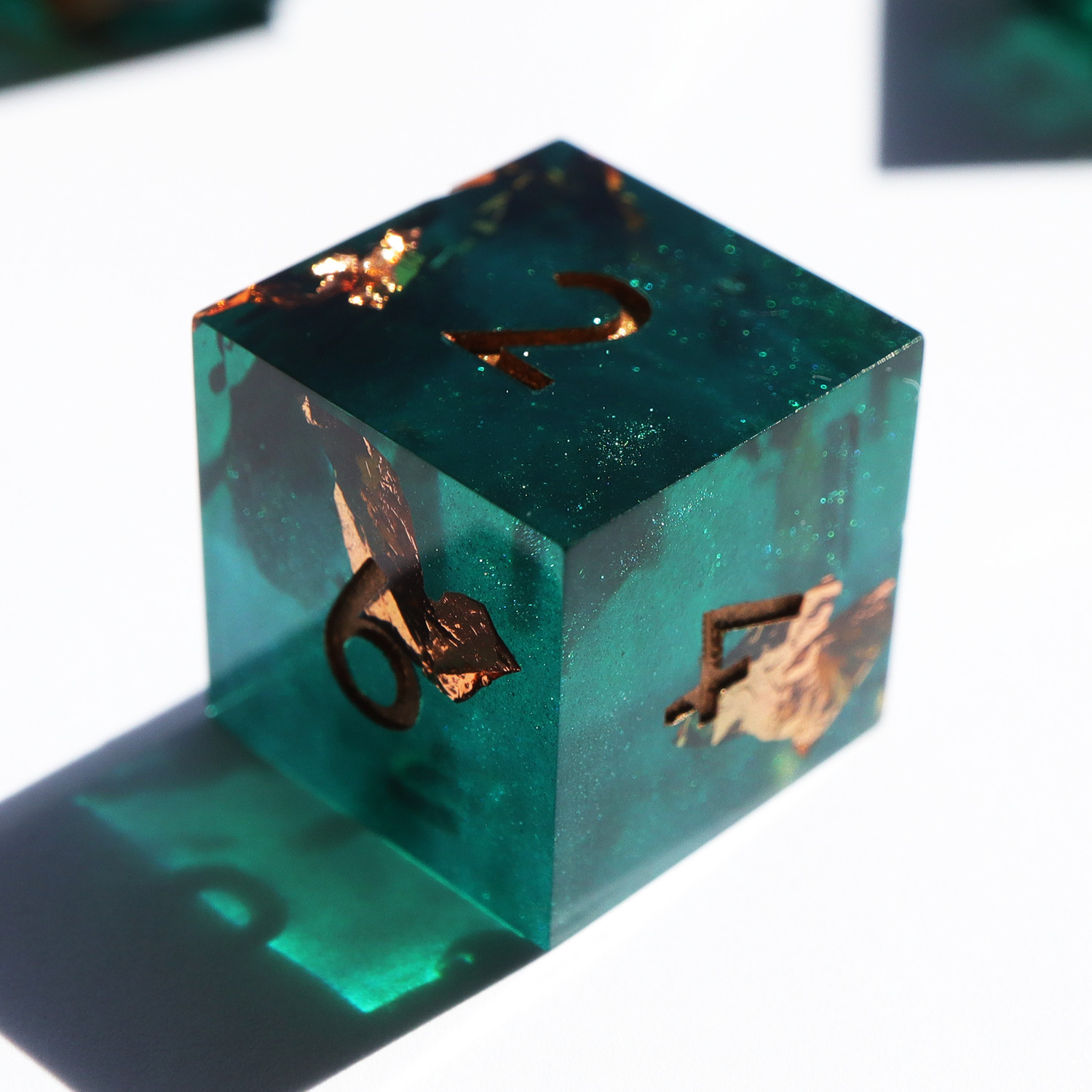 Single Decay Deco d6 on a white background. All the dice are a semi-opaque teal with sparkles and gold foil. The numbers on the dice are gold.