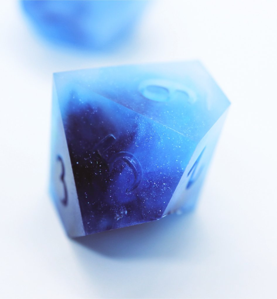 Closeup of a single D10 test design on a white background. The die is an opaque mix of light and dark blue resin with some sparkle. The numbers on the die are uninked.