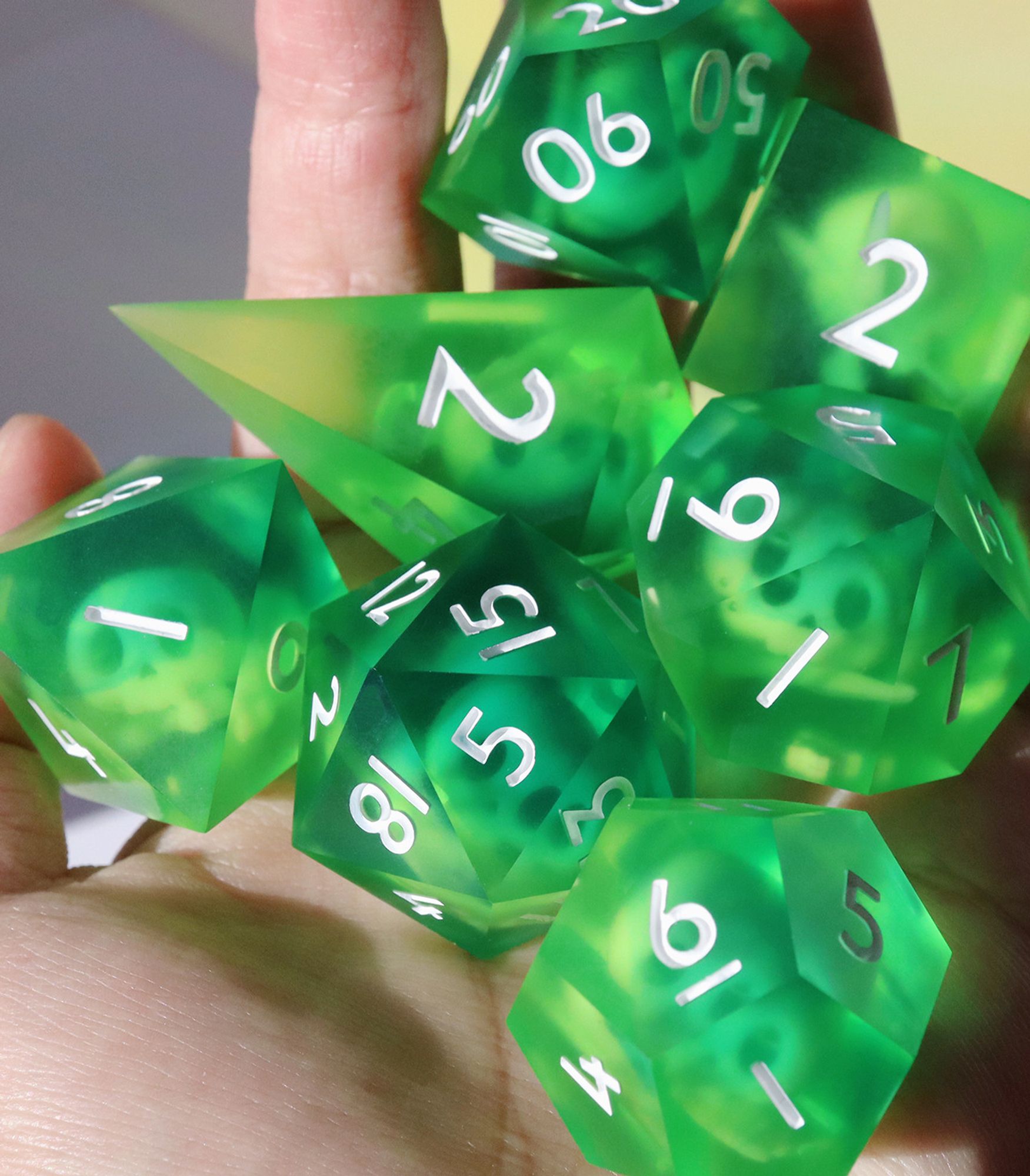 Full set of Gelatinous Cube dice in the palm of a hand. The dice are 40mm oversized dice that are a semi-opaque bright green with small bones and skulls inside them. Numbers on the die are white.