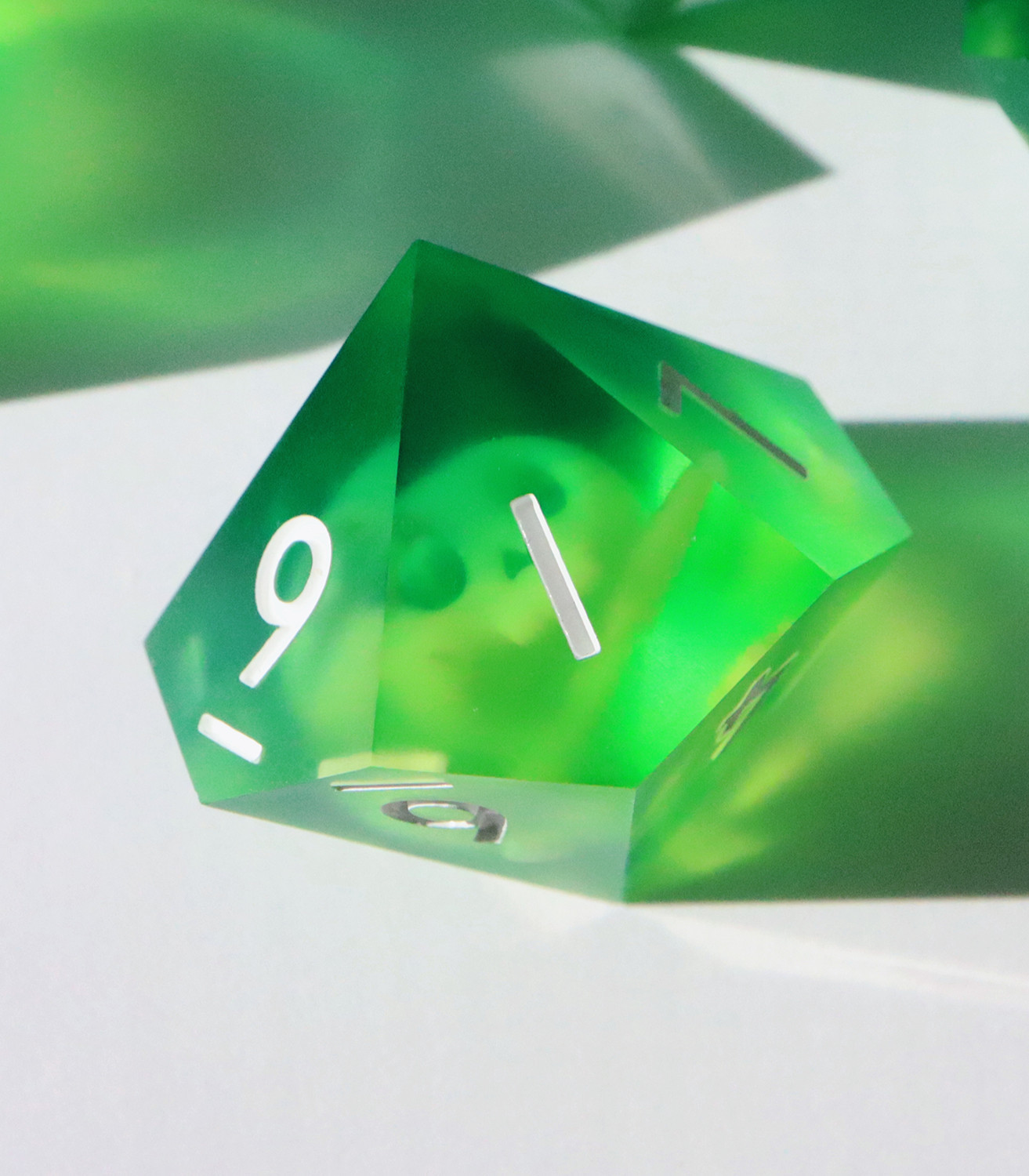 Closeup of the Gelatinous Cube D10 on a white background. The die is a semi-opaque bright green resin with floating inclusions of skulls and bones.