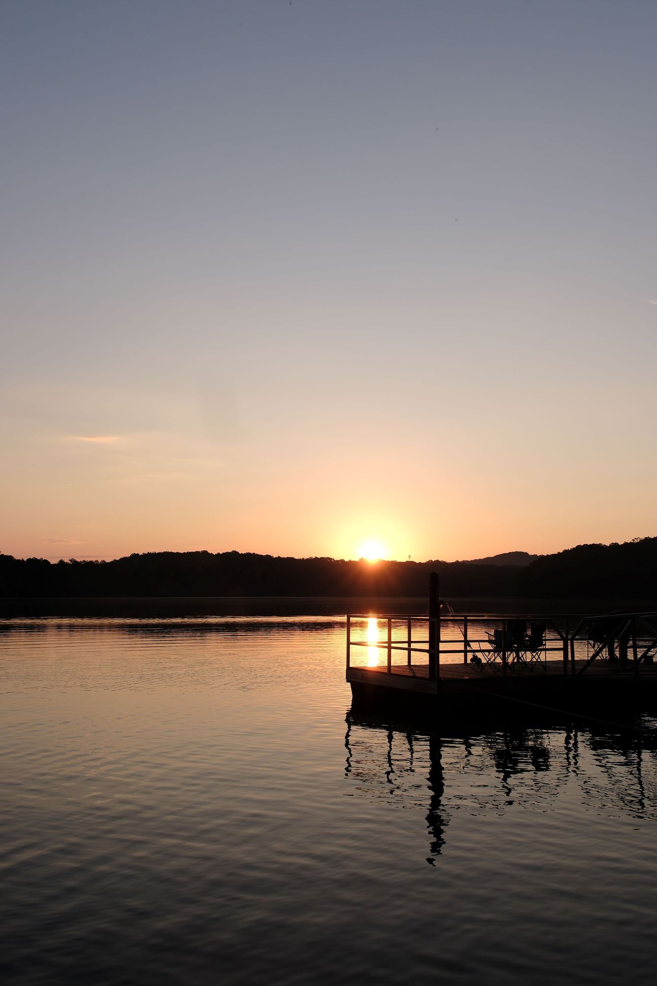 The sun is rising over a lake, the sky is just about to light up, a deck over a lake on the right