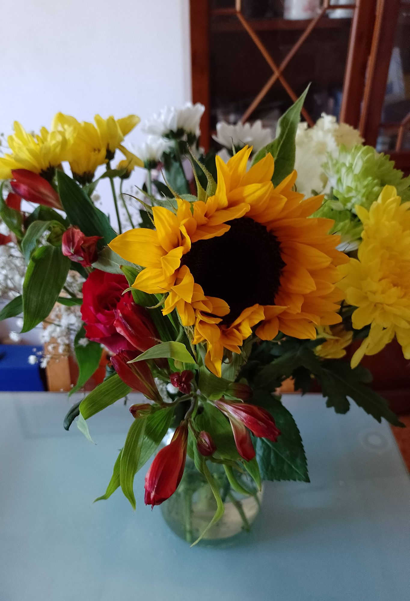 Bouquet of flowers on a dining room table. There are sunflowers, roses, lilies and  chrysanthemums in the arrangement.