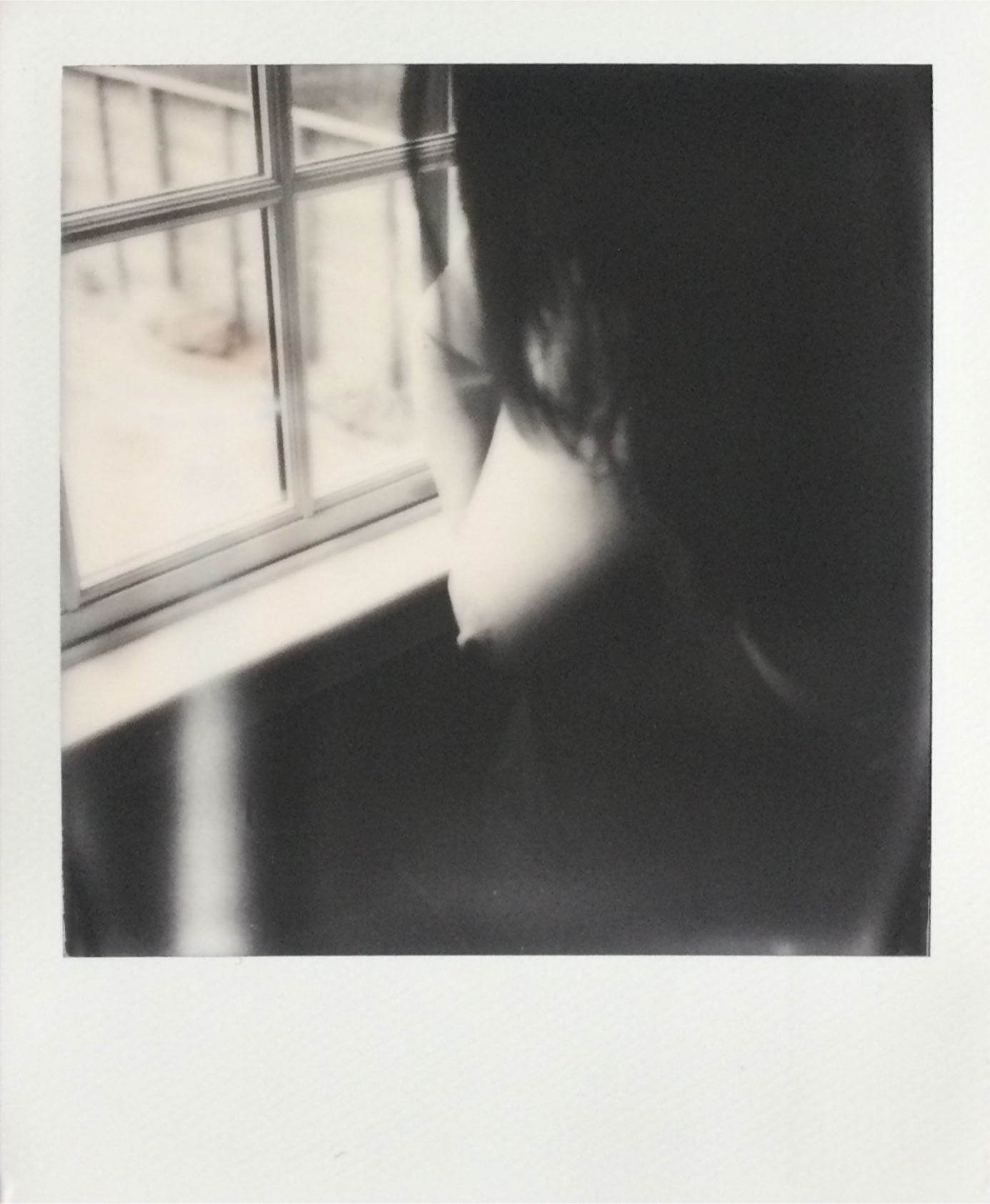 Black and white Polaroid of my nude torso by a window.  My long dark hair covers my face and my right boob is highlighted by the window light while the left boob and my lower torso are in shadow.