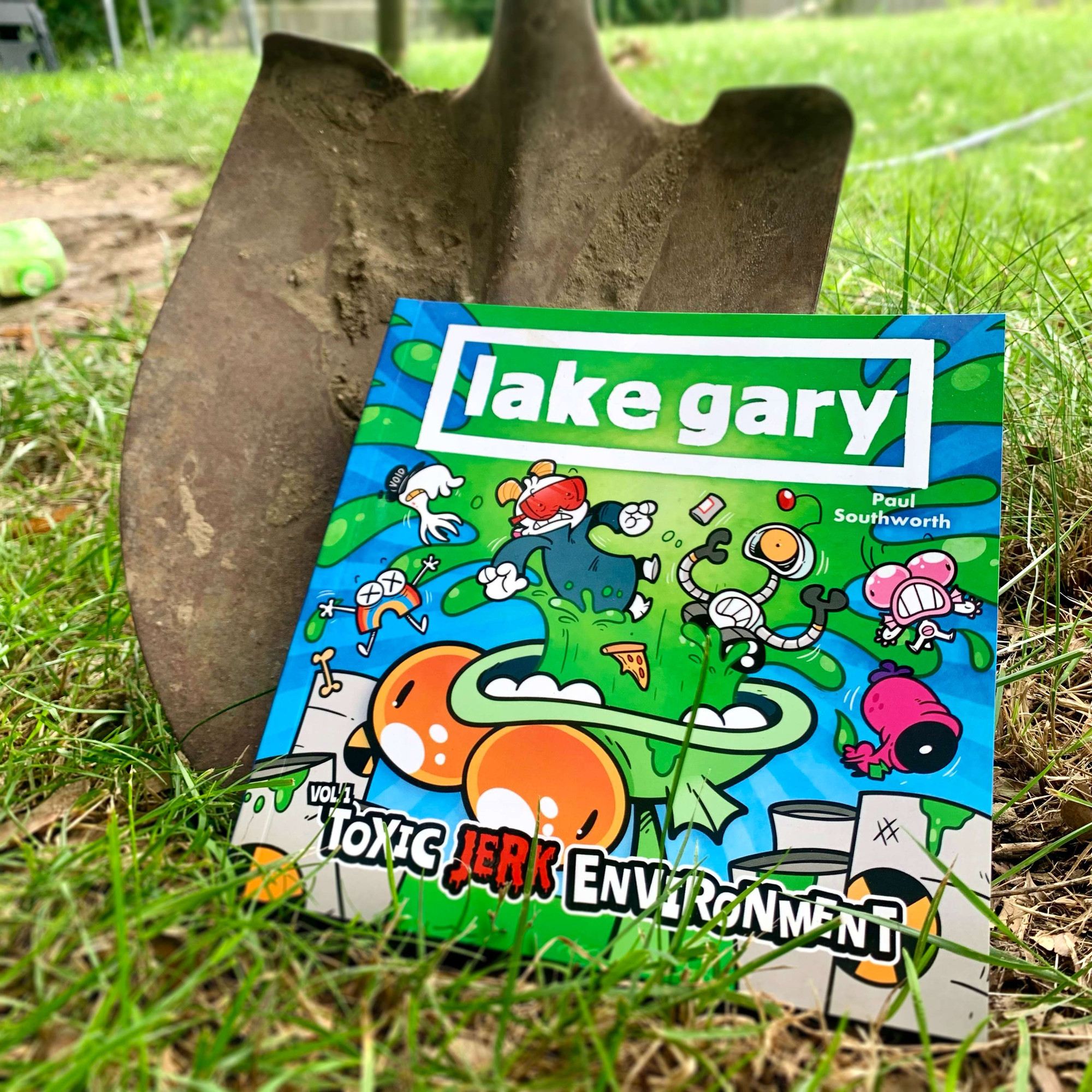 The LAKE GARY book sitting in the grass and leaning against a shovel