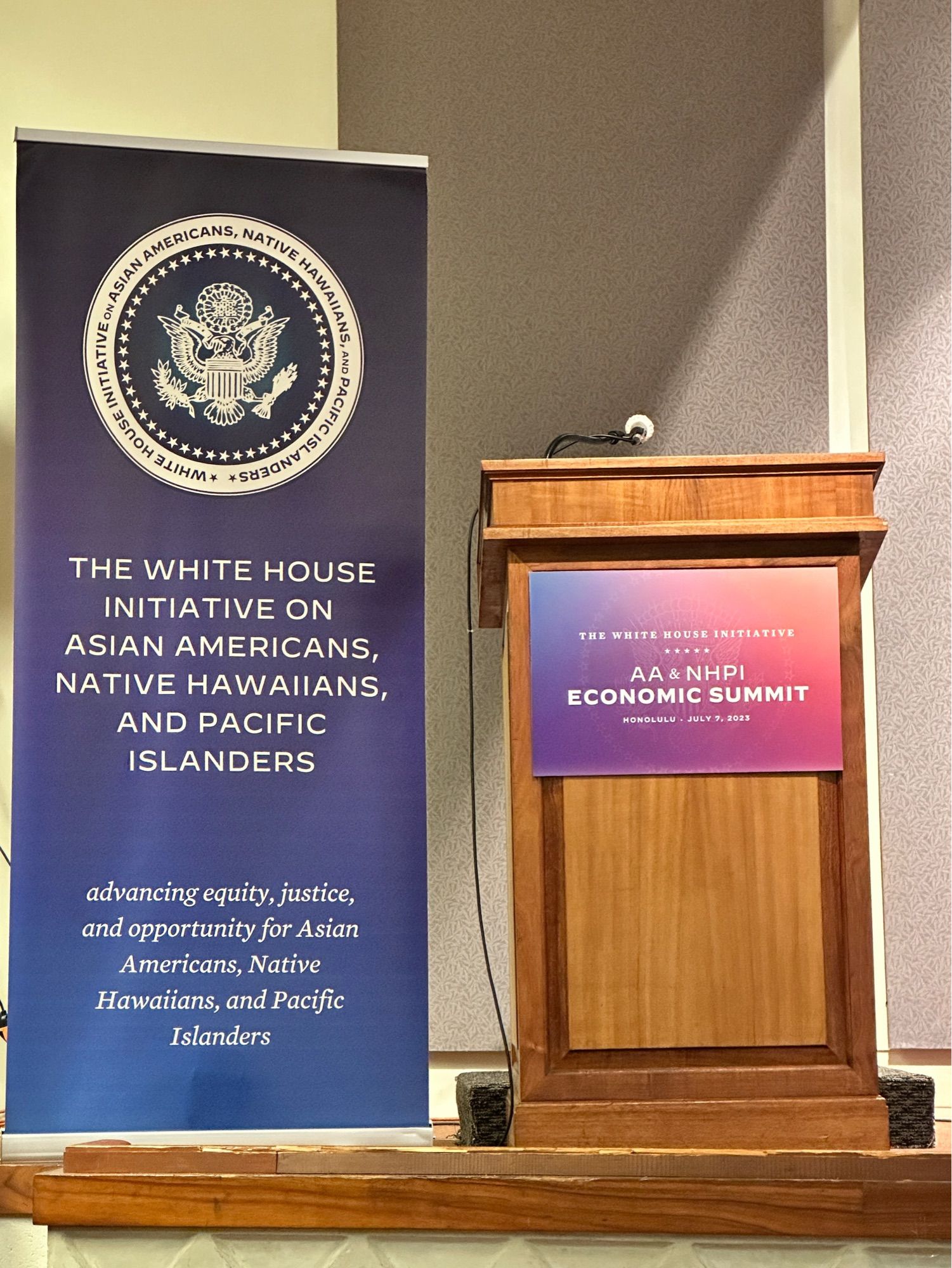 An upright banner for the White House Initiative on Asian Americans, Native Hawaiians, and Pacific Islanders, and a podium with a placard that reads AA & NHPI Economic Summit.