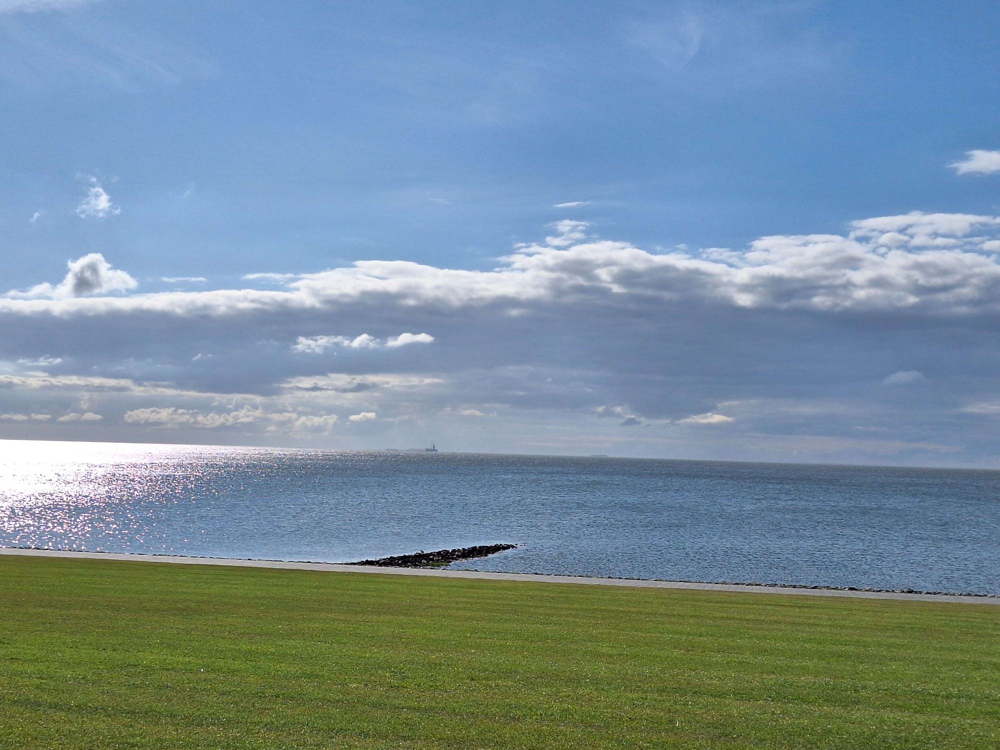 Blick auf die Nordsee. Mit Blauem Himmel und Wolken. Davor der grüne Rasen vom Deich.