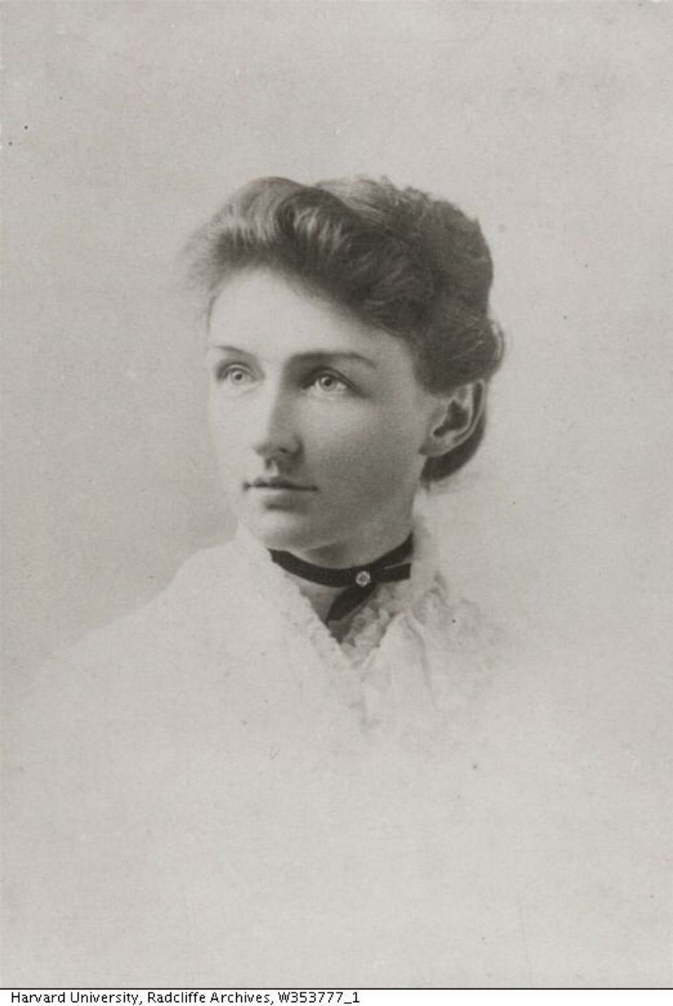 Black and white photo of Annie Jump Cannon. She wears a white blouse or jacket, with a frilly collar, and a black choker. Her hair is short, and she is looking to the left of the photographer.