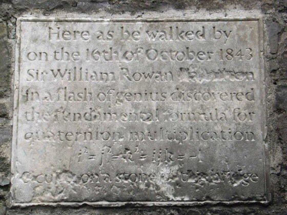 Color photo of a weathered stone plaque that reads "Here as he walked by on the 16th of October 1843, Sir William Rowan Hamilton in a flash of genius discovered the fundamental formula for quaternion multiplication..."