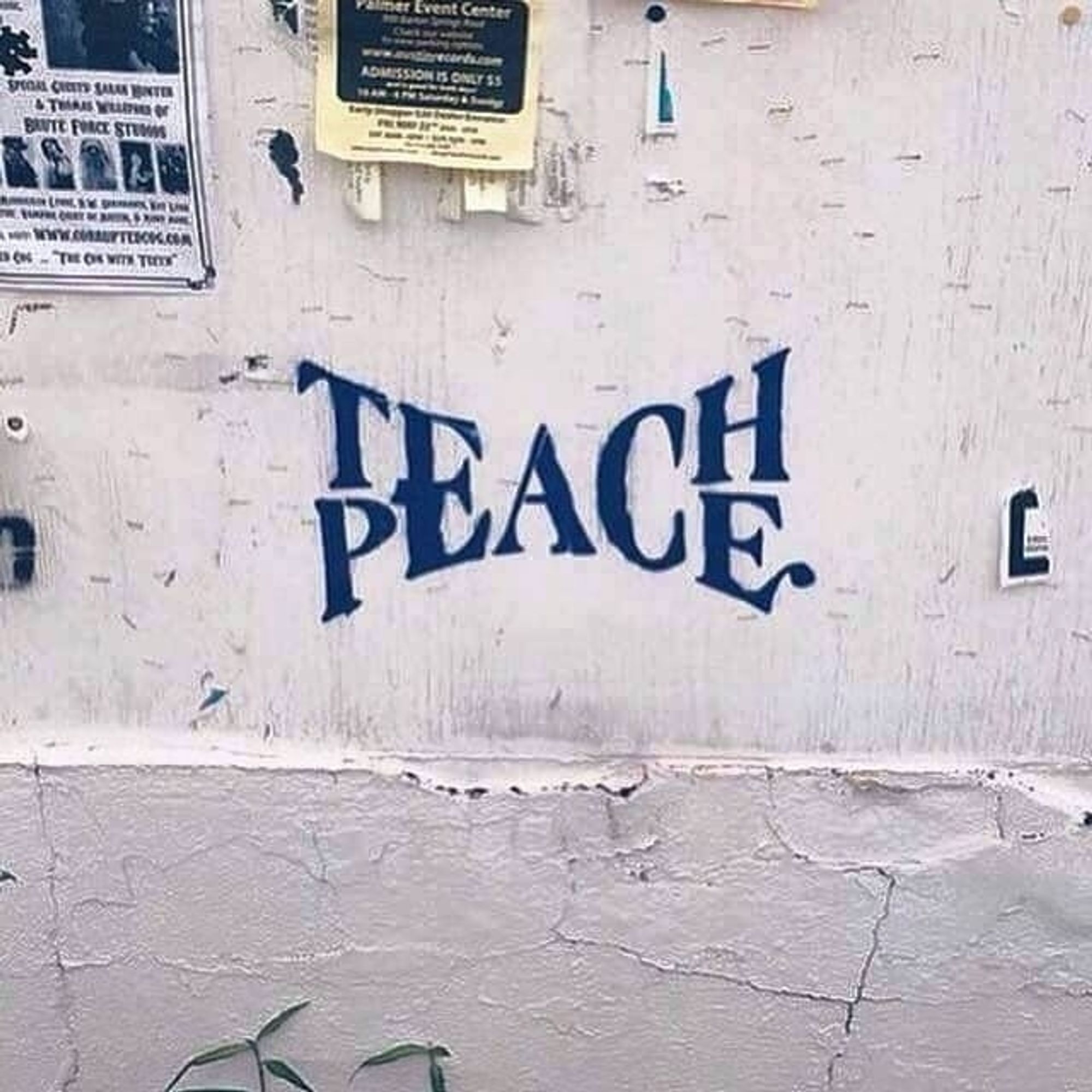 Auf einer weißen Wand ein Graffiti in blau.
In der Mitte steht EAC. Darüber die Buchstaben T am Anfang und H am Ende, sodass das Wort Teach ergibt. Darunter am Anfang ein P und am Ende ein E, das Wort ergibt Peace. Es steht dort also Teach Peace.