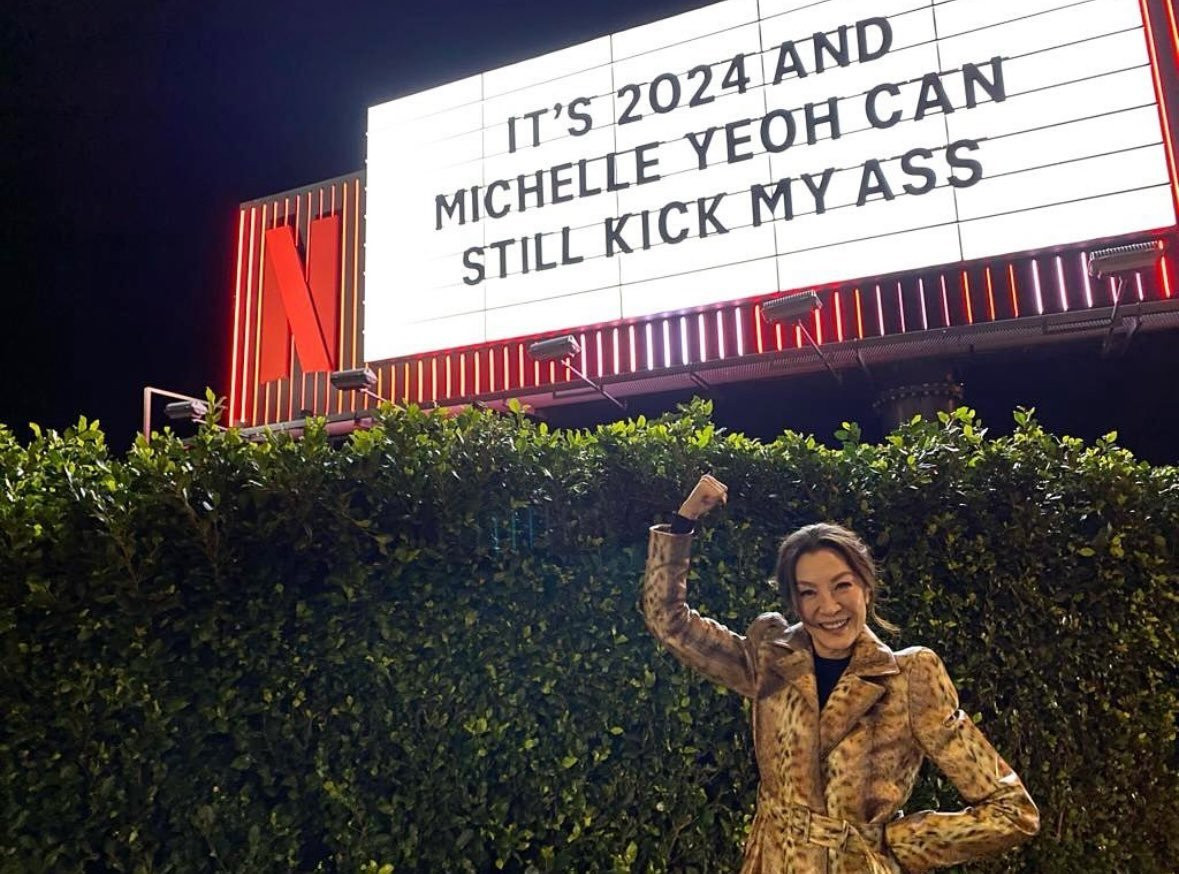 Michelle Yeoh posing in front of a theater marquee reading

it's 2024 and 
Michelle Yeoh can
still kick my ass