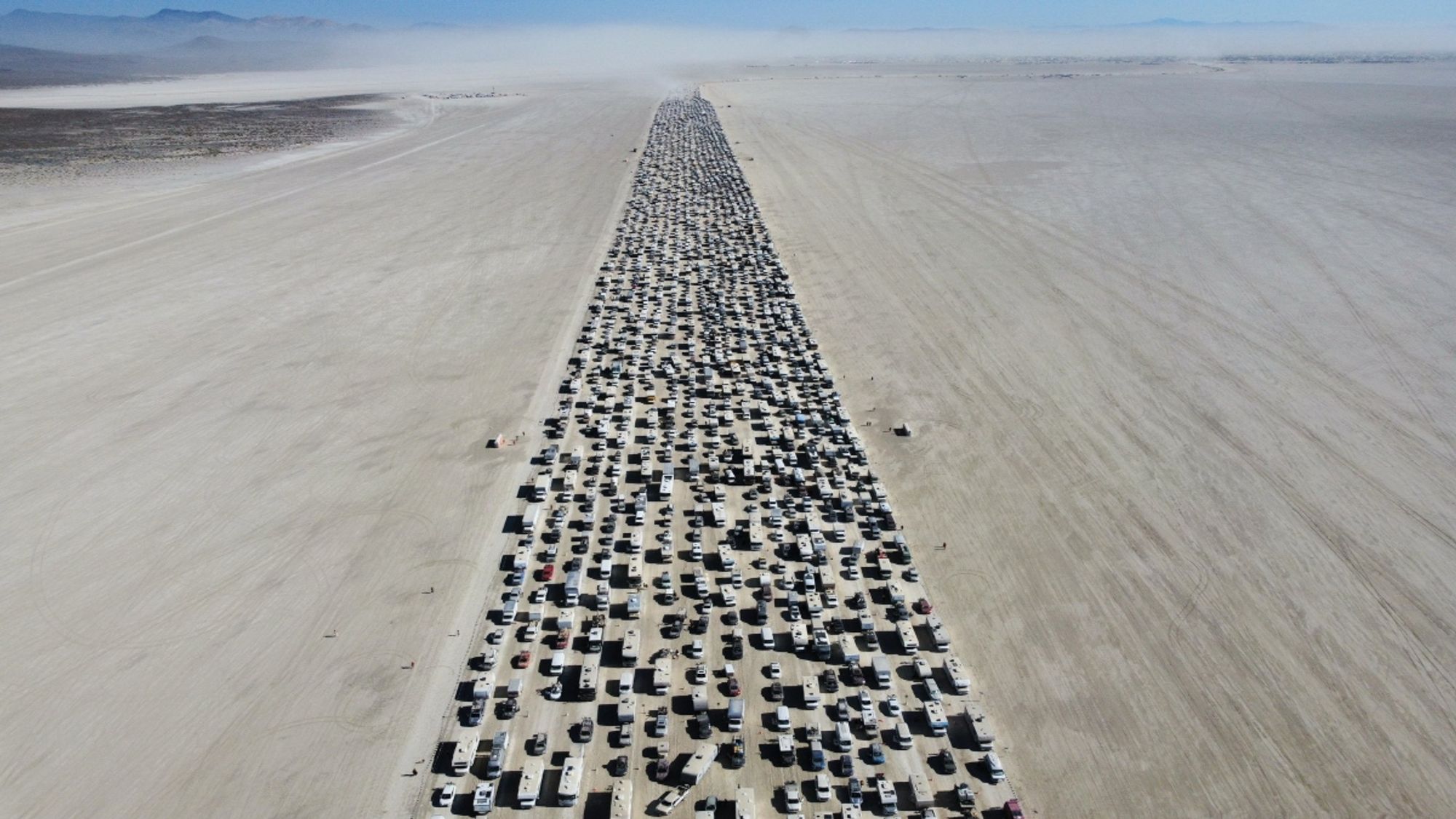 ariel photograph of vehicles leaving burning man, a packed ribbon of cars stretching off to the horizon