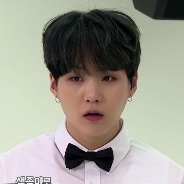 Yoongi wearing a white long sleeved shirt and a black bowtie. His hair is dark/black.