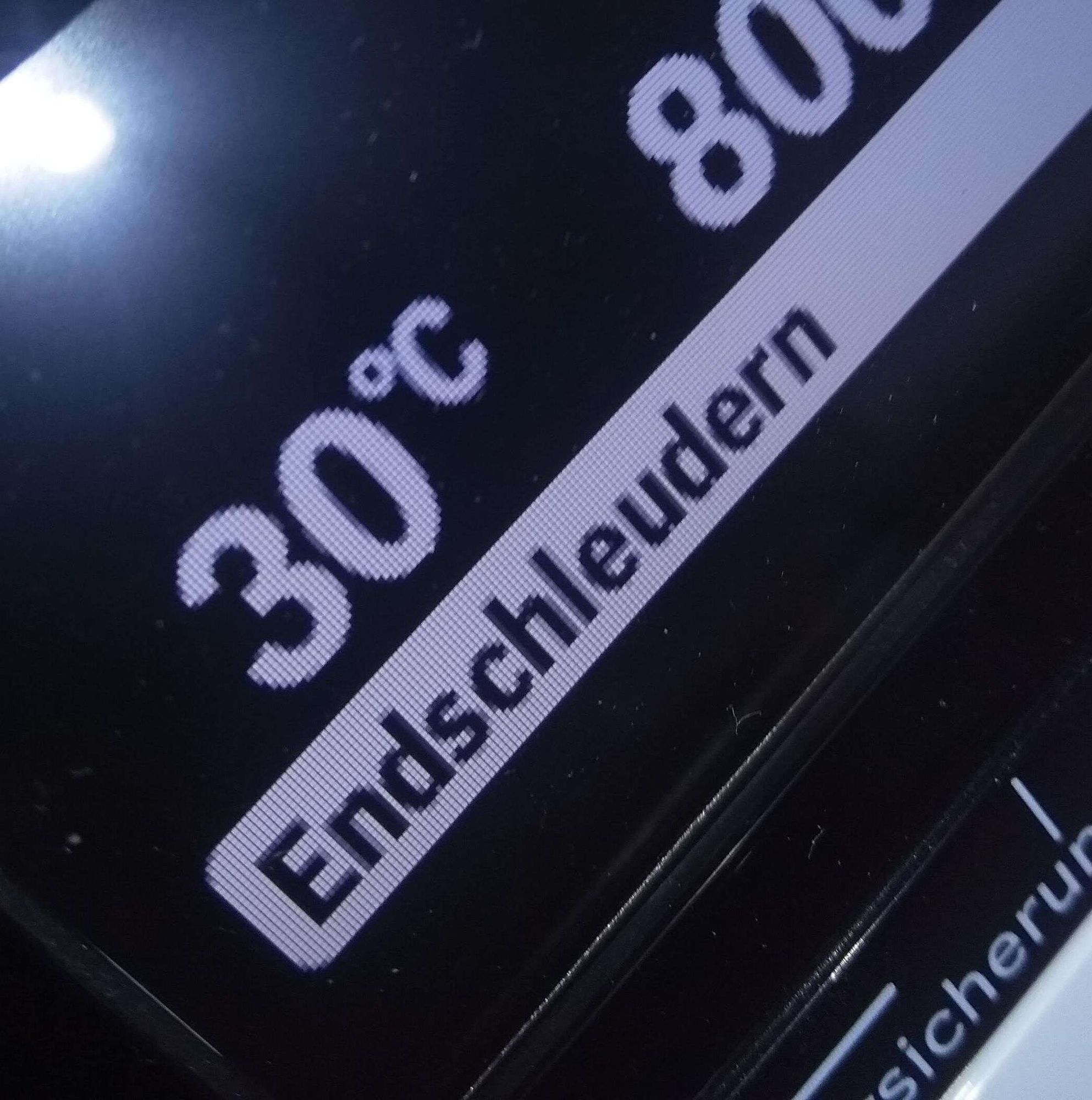 Display einer Waschmaschine in Nahaufnahme. Weiß auf Schwarz teilt die Maschie mit, dass sie bei 30 Grad Celsius wäscht und sich gerade mit Endschleudern befasst.