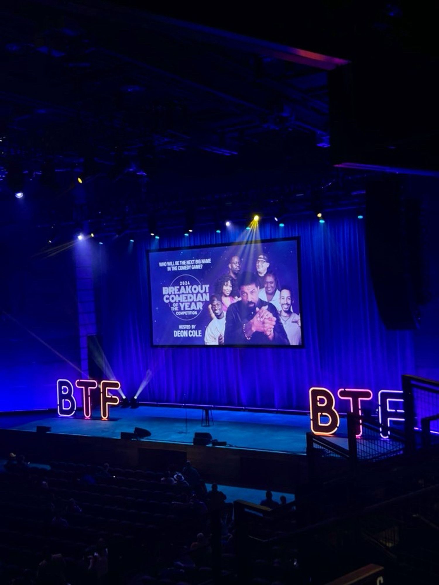 An image of the Anthem, a music venue in Southwest DC, showing an empty stage and neon letters spelling BTF, for the Because They’re Funny Comedy Festival