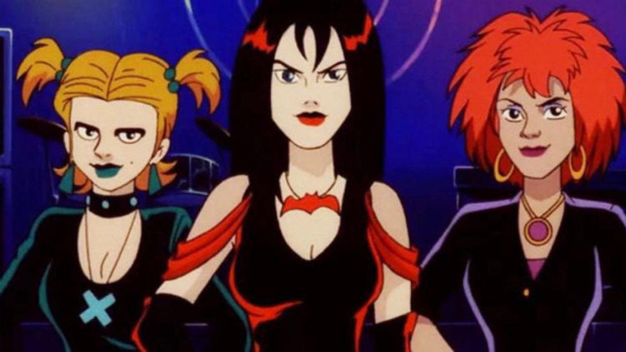 A screenshot of the “Hex Girls” from Scooby Doo. A woman on the left dressed in green with green earrings, lipstick, necklace and in blonde pigtails. A woman in the middle with long hair, a red dress, red lipstick and a red bat necklace. A woman on the right with red hair, gold hoop earrings, a pendant necklace and wearing purple.