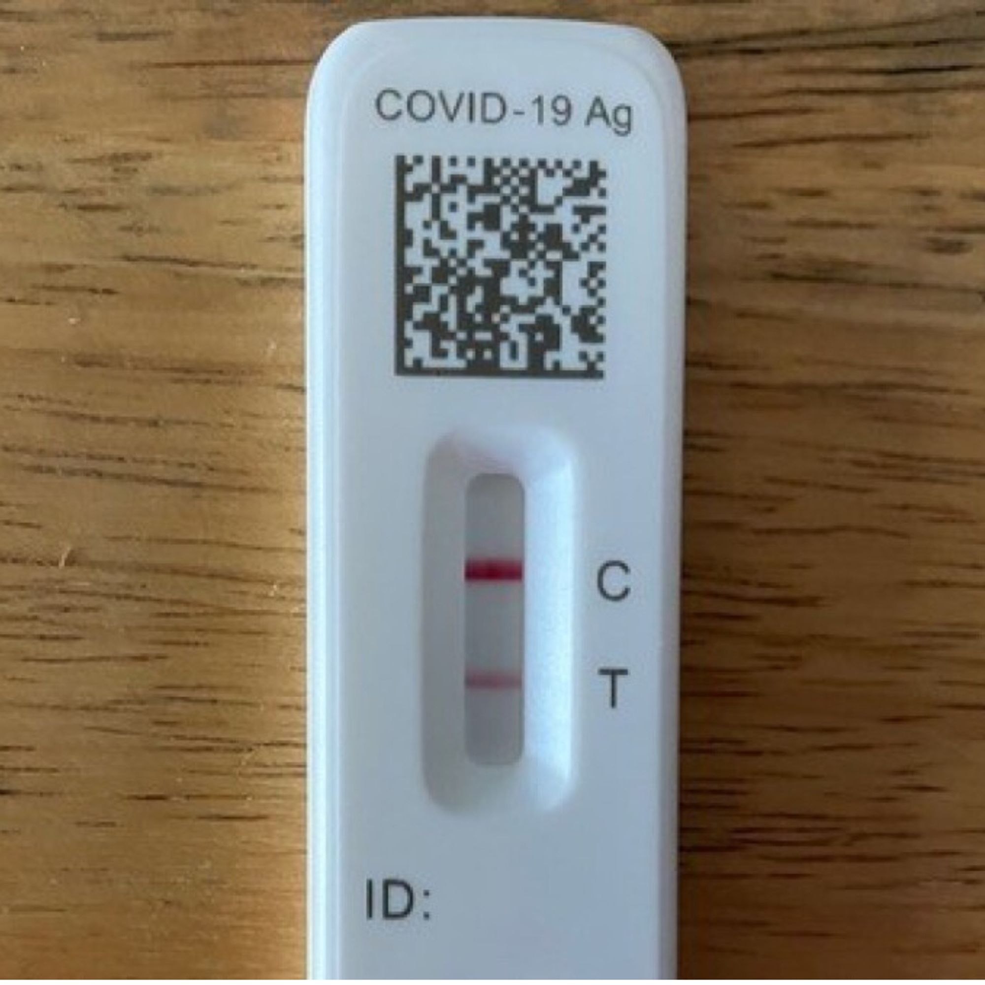 On top of a brown wooden table is a COVID test with two lines indicating it is positive.