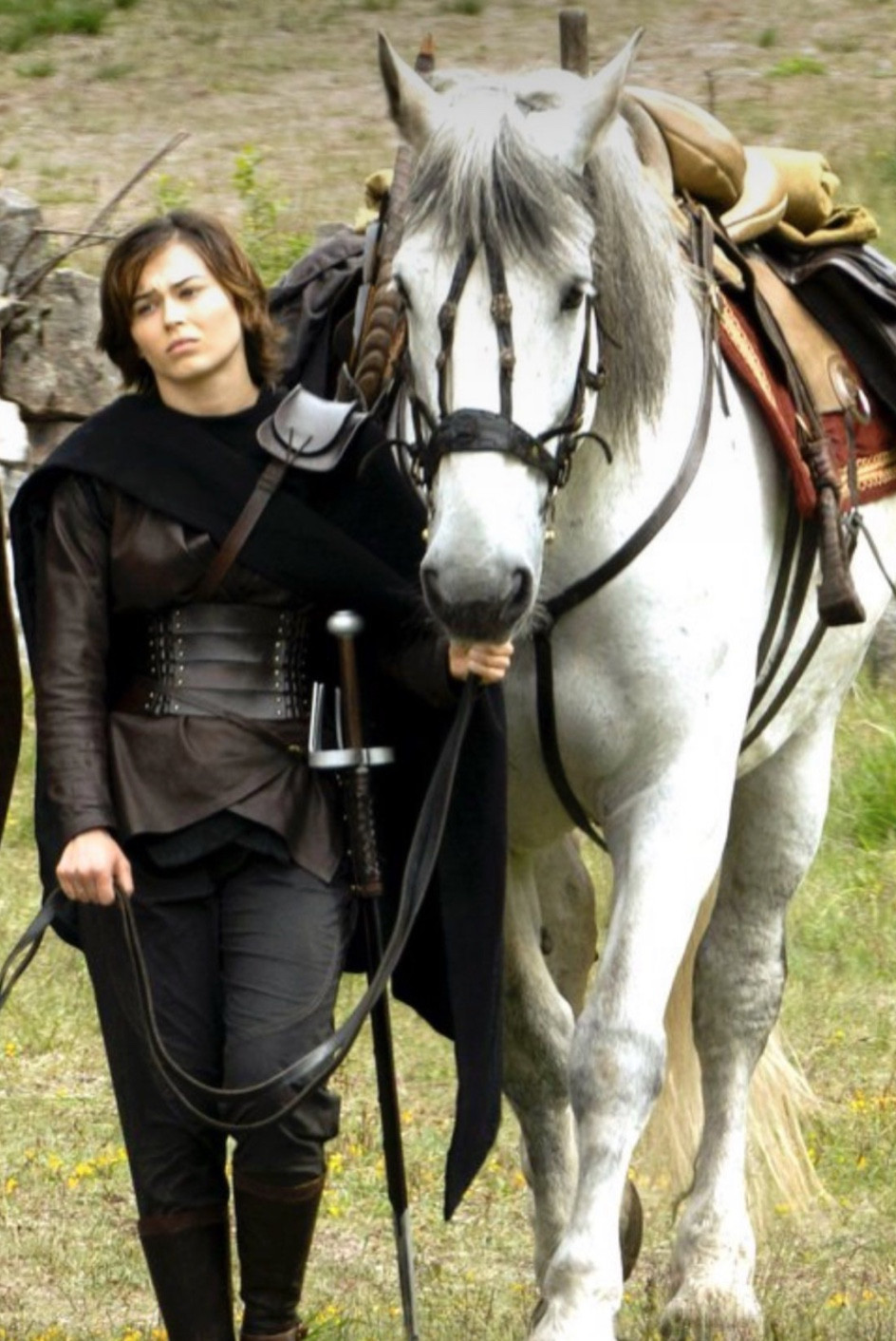 Ruby Cruz wearing fantasy clothing/armor with a sword as Kit in Willow 2022 holding the reigns of a white horse 