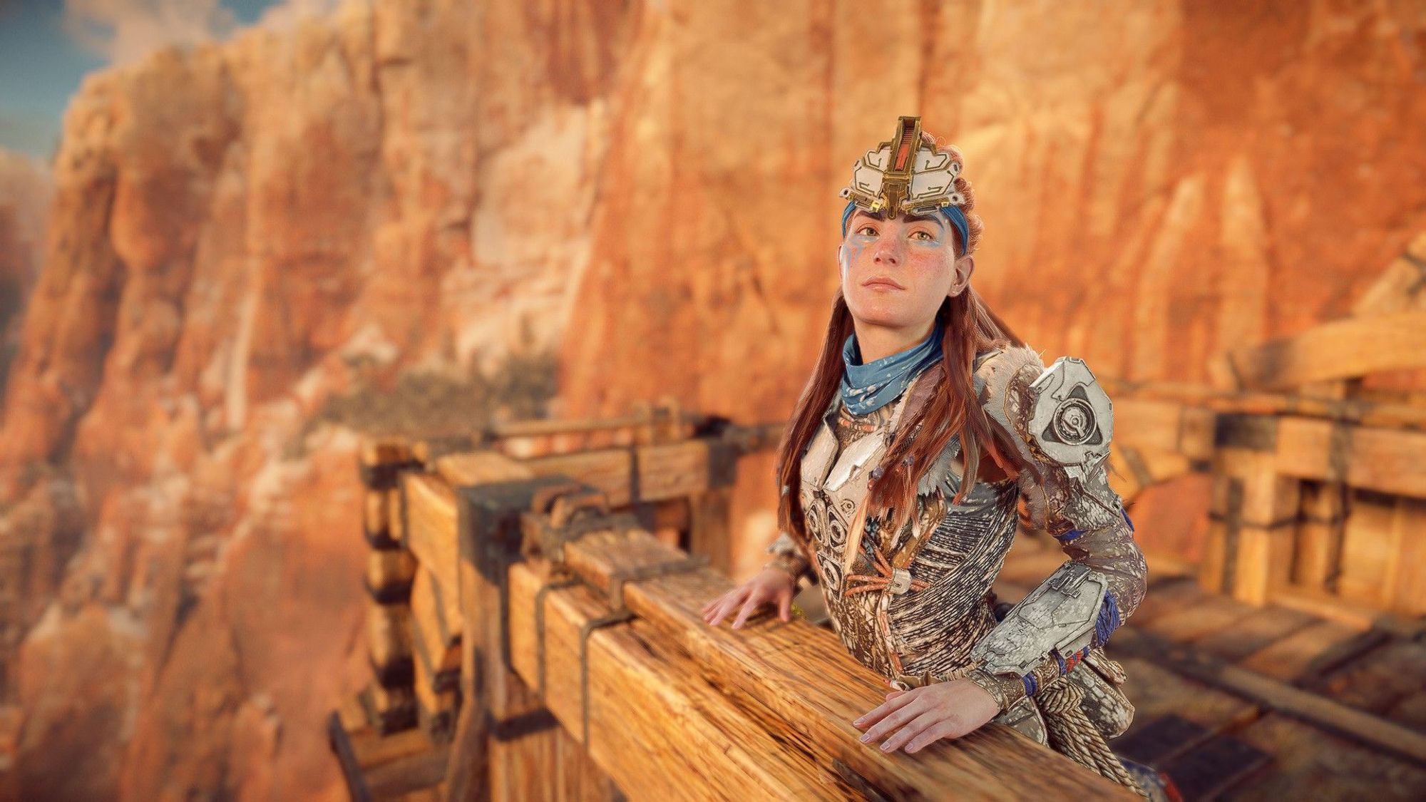 Aloy with her hands on a wooden rail, looking toward the camer in a pensive manner.