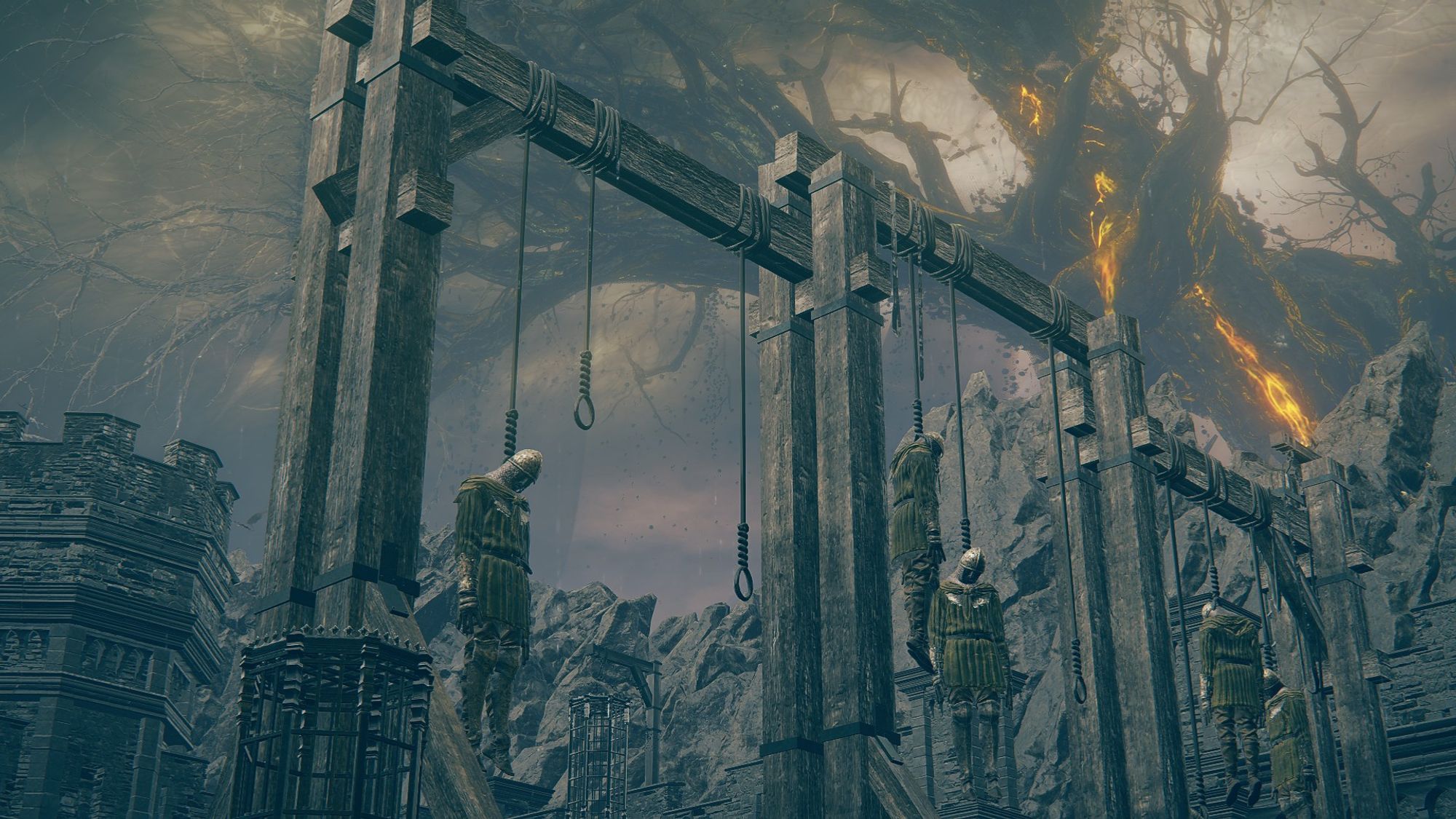 Elden Ring: Shadow of the Erdtree DLC screenshot; an up angle shot of the gallows in the courtyard of the fort. Four soldiers of the opposing army hang there, with the Shadu Tree in the far background.