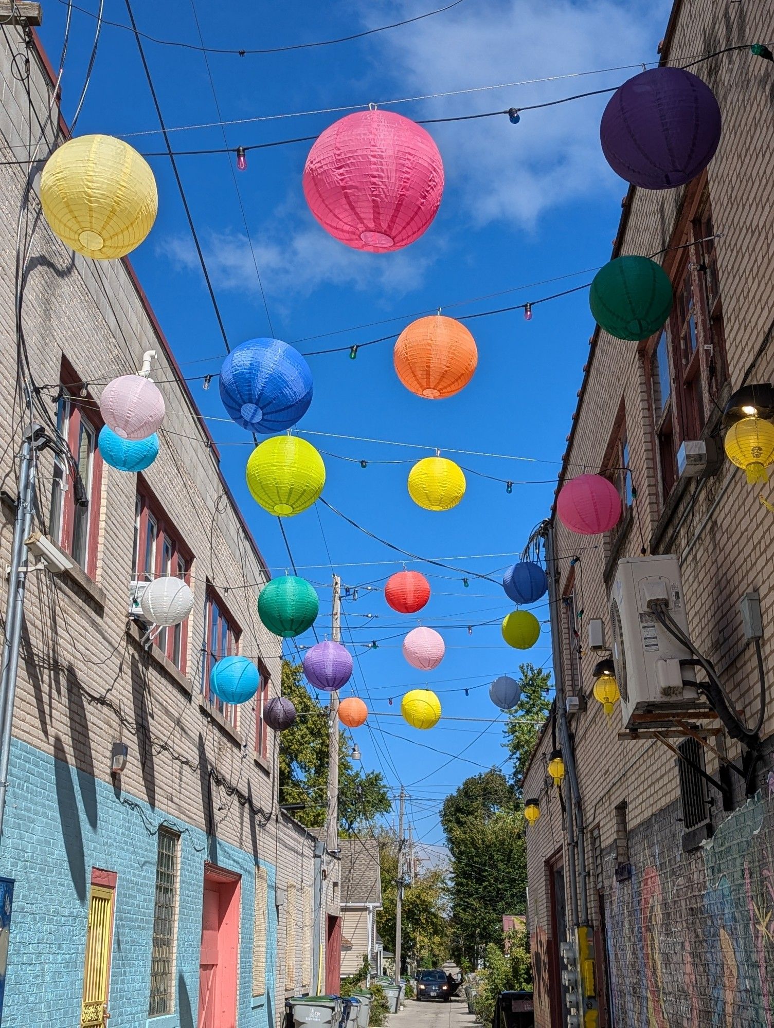 Alleyway between two brick buildings with multi colored paper lanterns strung between on rope.