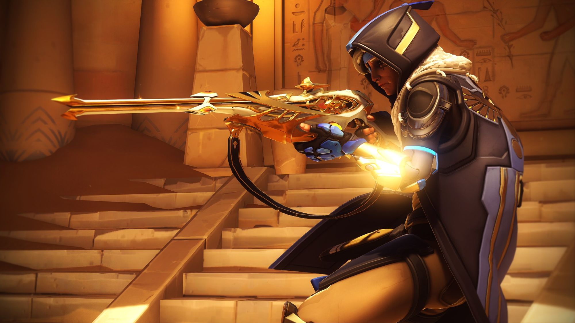 Overwatch 2 screenshot of Ana in her basic Overwatch 2 outfit. It is a tactical suit with a long blue duster with hood, a scarf that looks similar to a keffiyeh, an eye patch and a hijab under her hood. Her suit underneath is beige. She has a very ornate white and gold-detailed sniper rifle with crystal details. The shot is in profile from her left side, and she's holding the gun out straight. She seems to be in some Egyptian tomb.