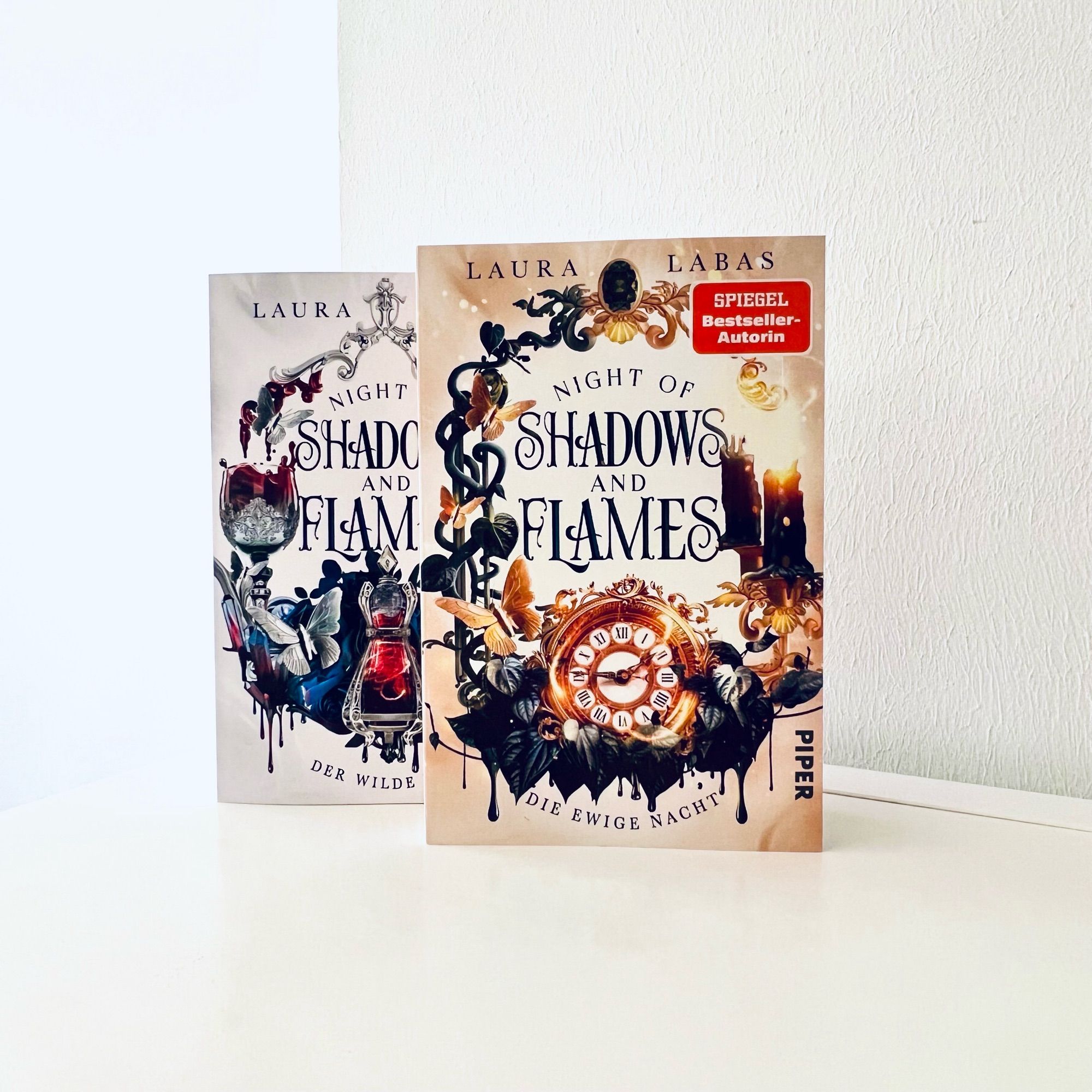 Das Bild zeigt die beiden Bände der Dilogie »Night of Shadows and Flames« von Laura Labas nebeneinander stehend. Beide Cover sind mystisch gestaltet Band 1 hat eine silbrig-weiße, Band 2 eine gelbgoldene Farbgebung.