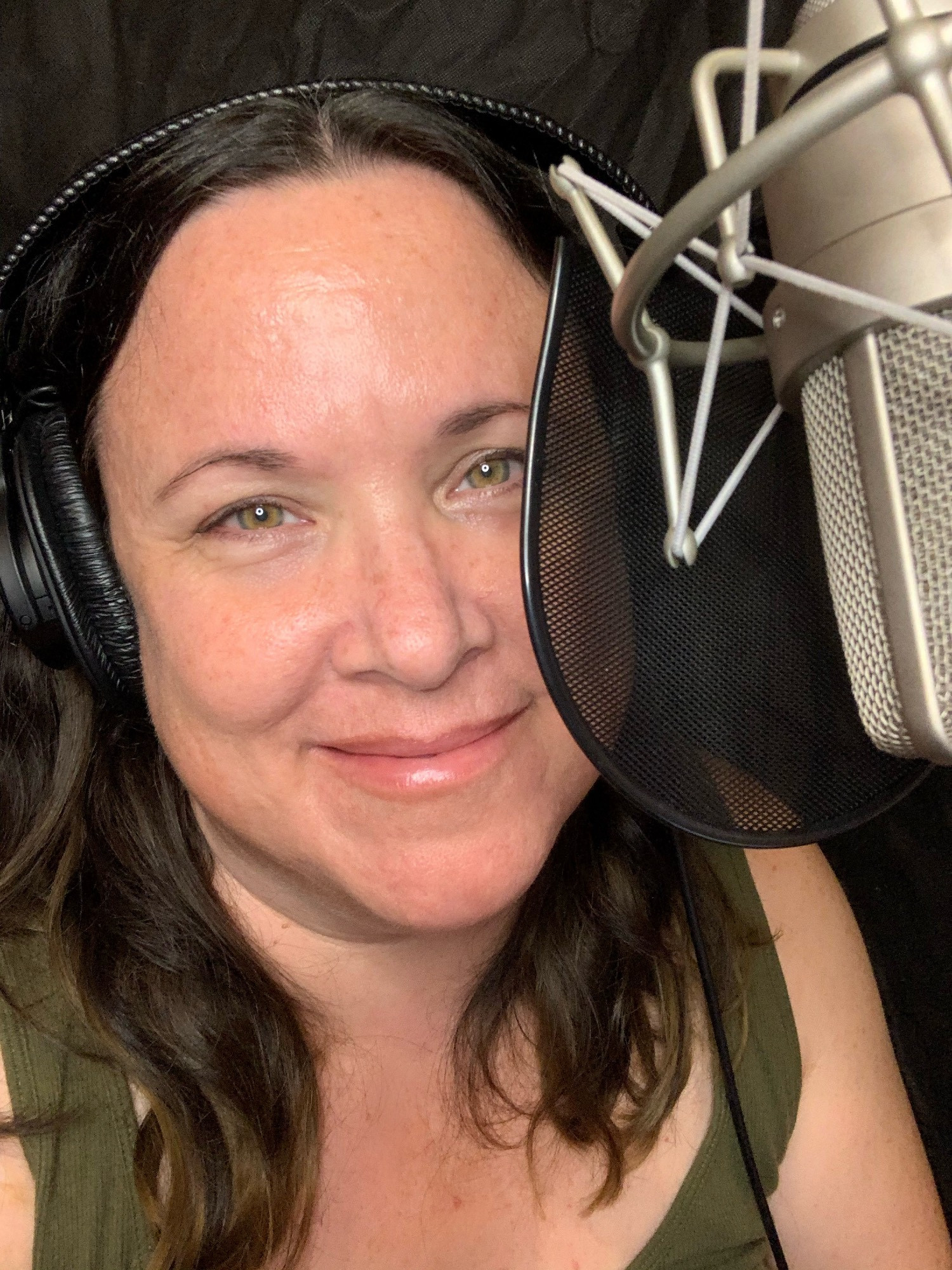 Selfie of me in my booth behind the microphone. Brunette hair just below the shoulders, yellow-green hazel eyes and wearing an olive green tank top.