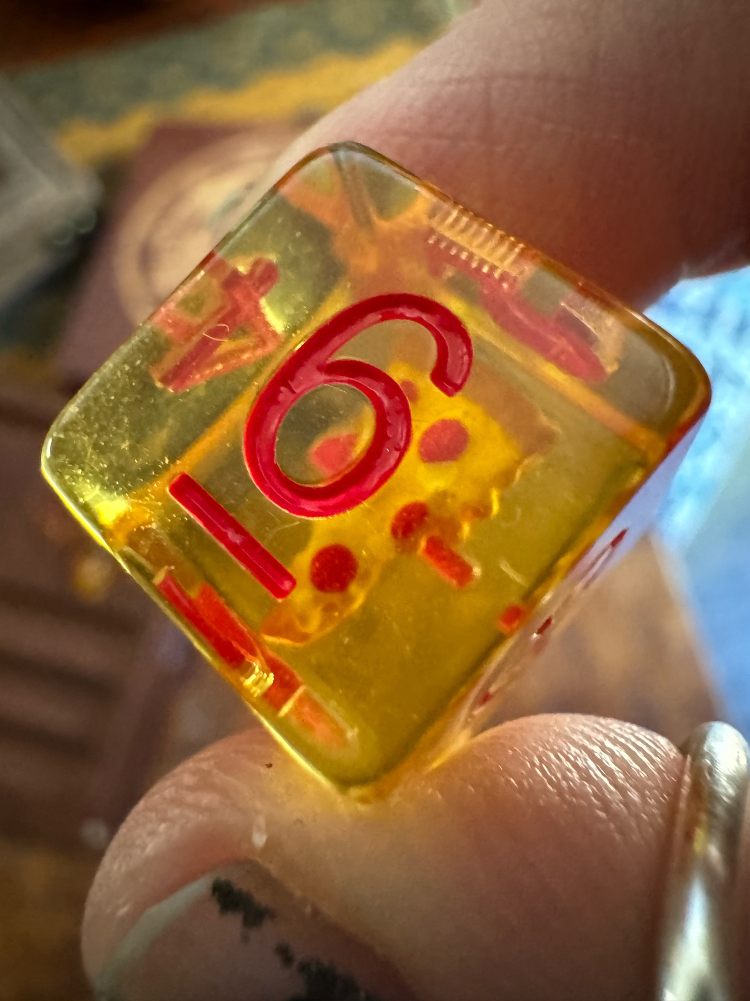 A close-up of the D6 die, transparent, yellow, with red numbering, showing a clear view of the tiny slice of pepperoni pizza at the center.