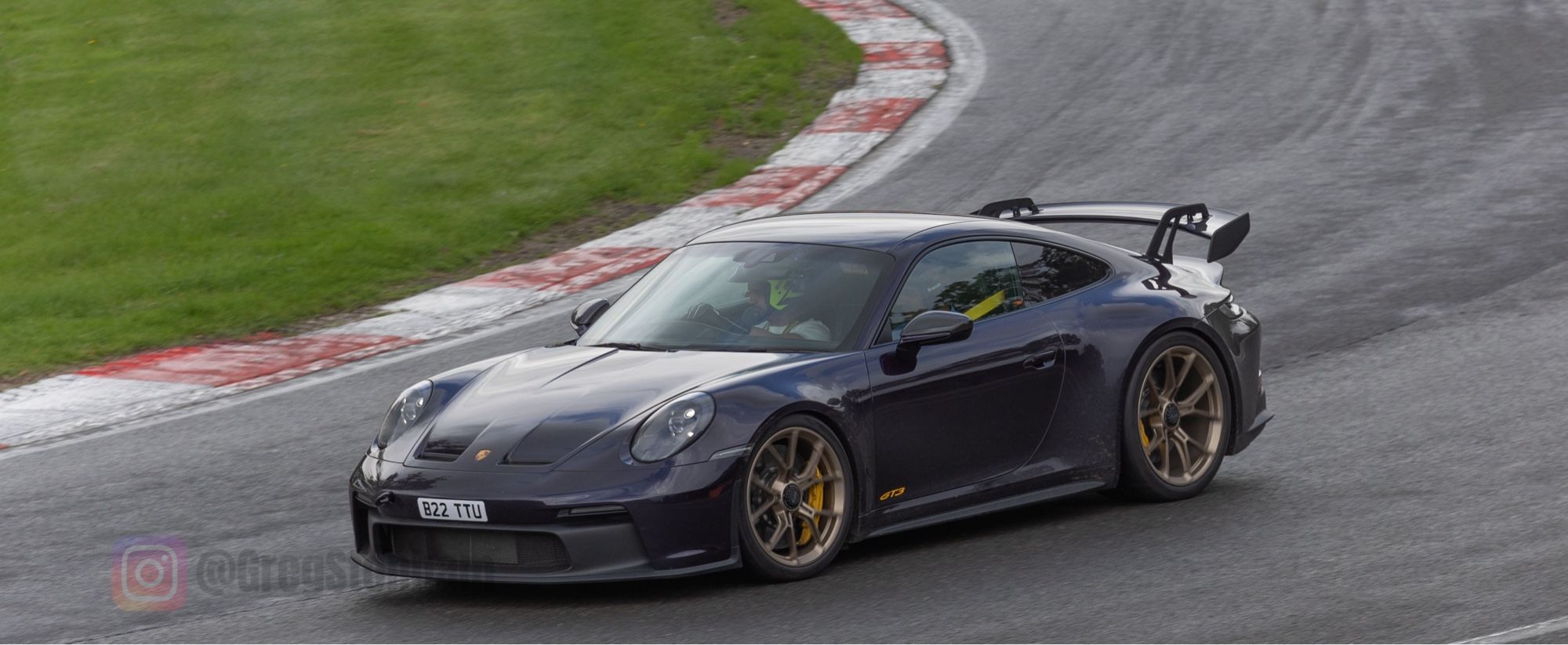 Porsche GT3 rounding druids corner at Brands Hatch. The car is glistening from Polish, the track shiny from rain.