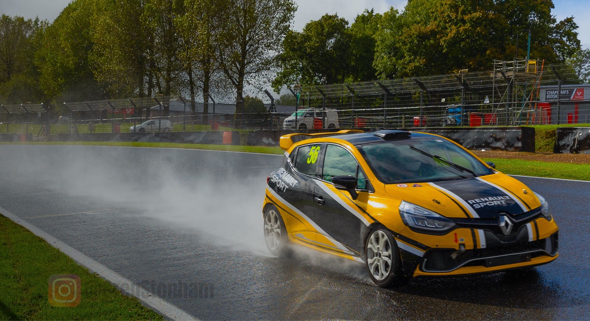 Renault Clio RS, in race livery with number 56, flat out down Brabham Straight at Brands Hatch. It’s raining, and the speed of the car is throwing water in the air in its wake.