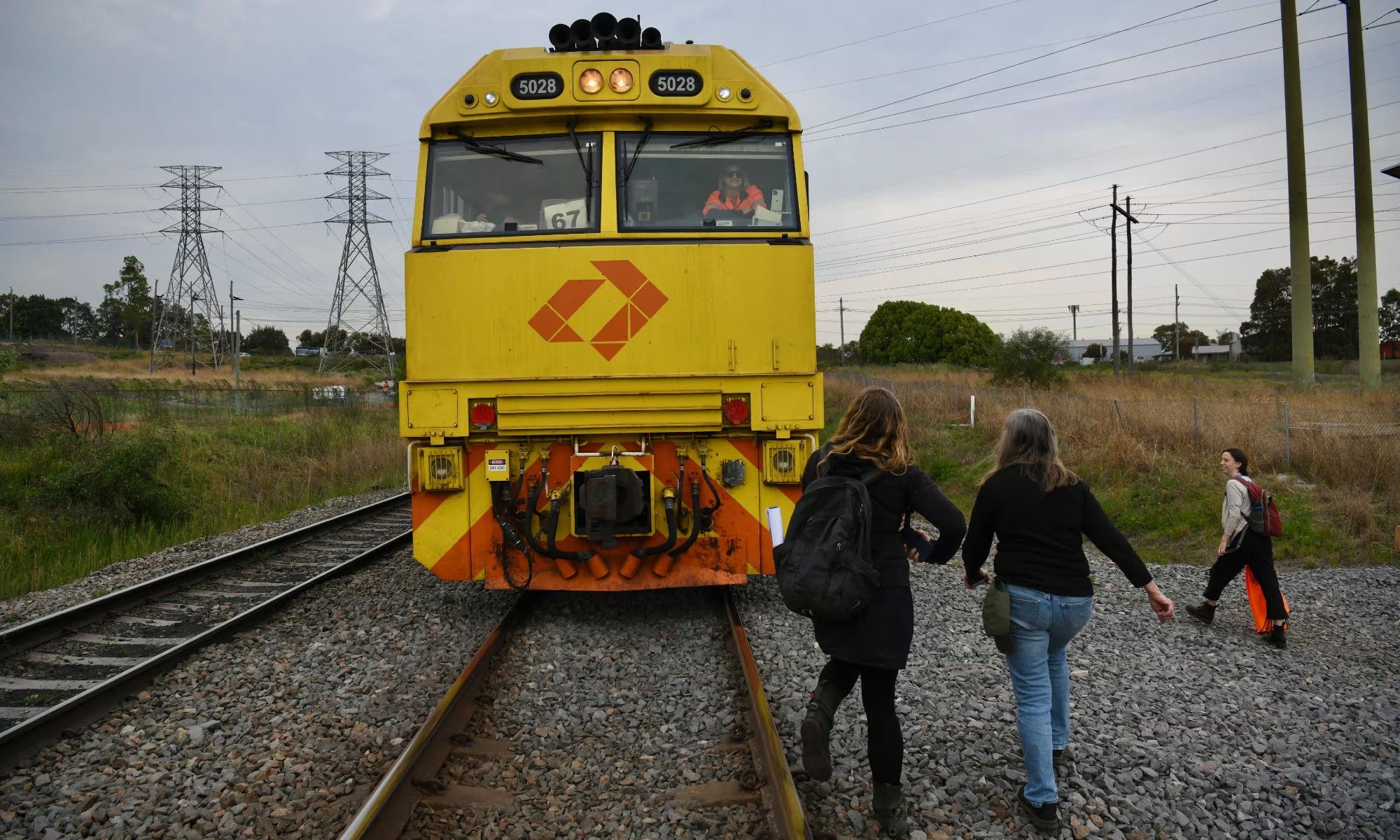 Some of the climate protesters on the train tracks in front of a large yellow train, and the driver sitting behind the controls of the train, smiling.