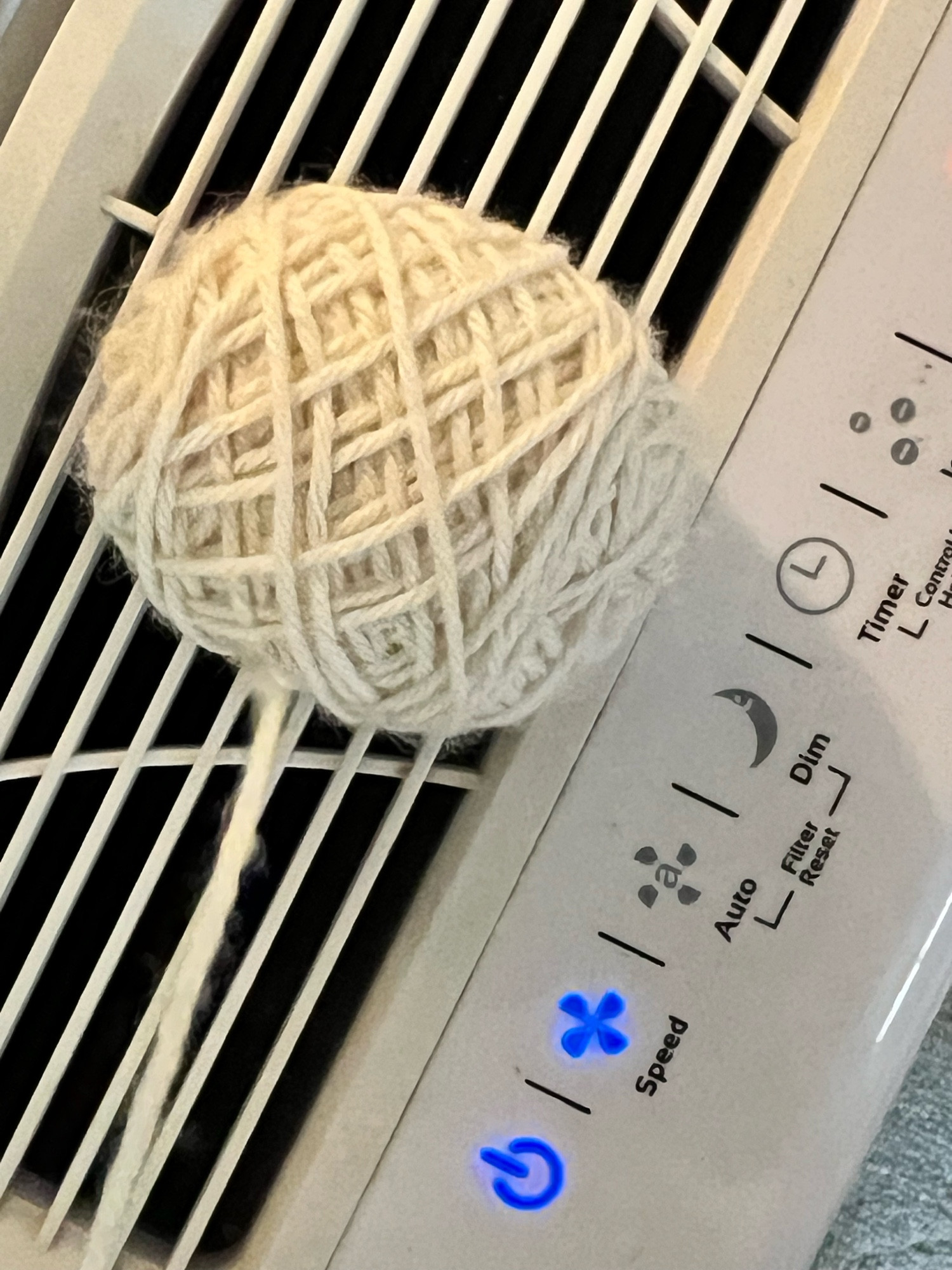 A ball of butter baby alpaca yarn in natural white - mid-knitting mittens, sitting on an air purifier, drying off after have hot black coffee poured (spilled) into the caverns of wound yarn. Clean air saves lives and 🧶