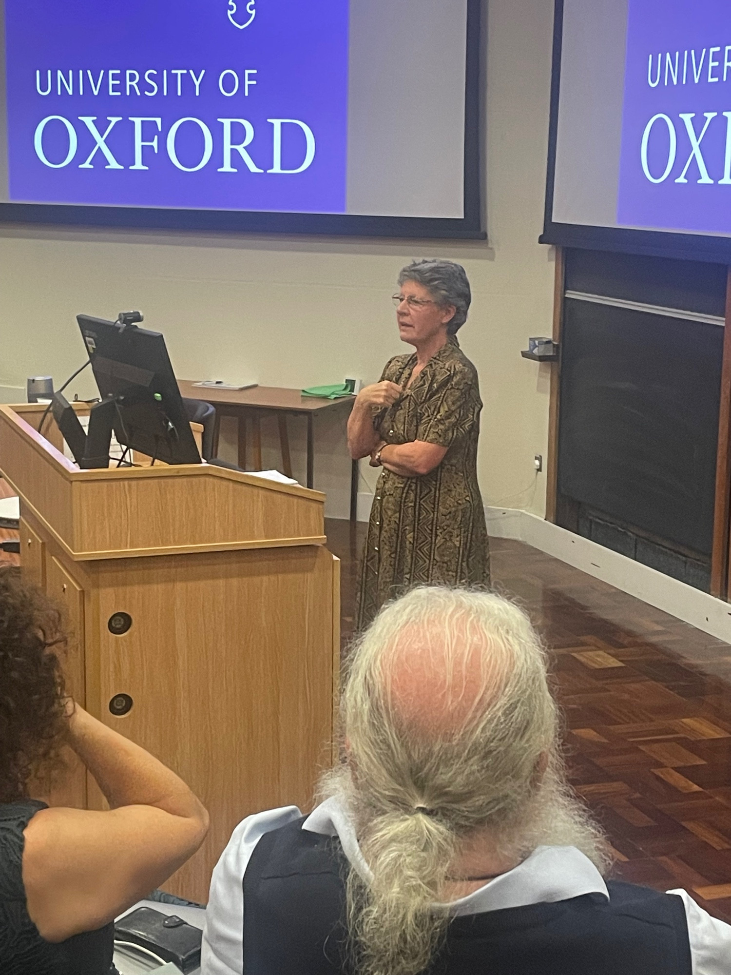 Jocelyn, wearing a gold and black dress, addresses an audience from a lecture theatre podium. 