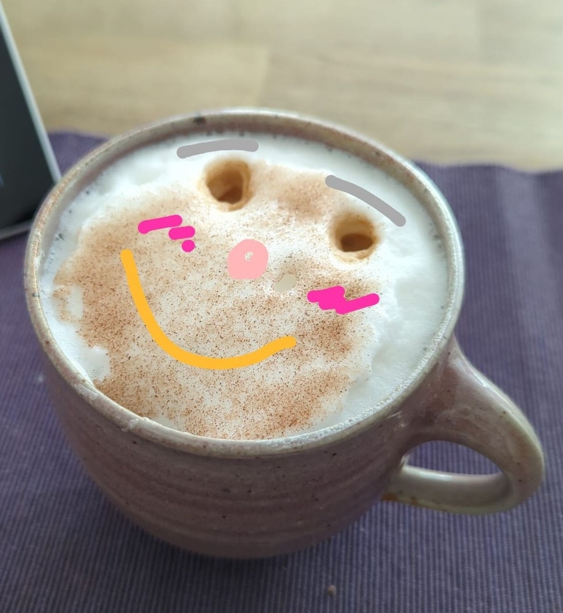 Eine Tasse Milchkaffee, auf dem Schaum ist ein Gesicht gemalt.