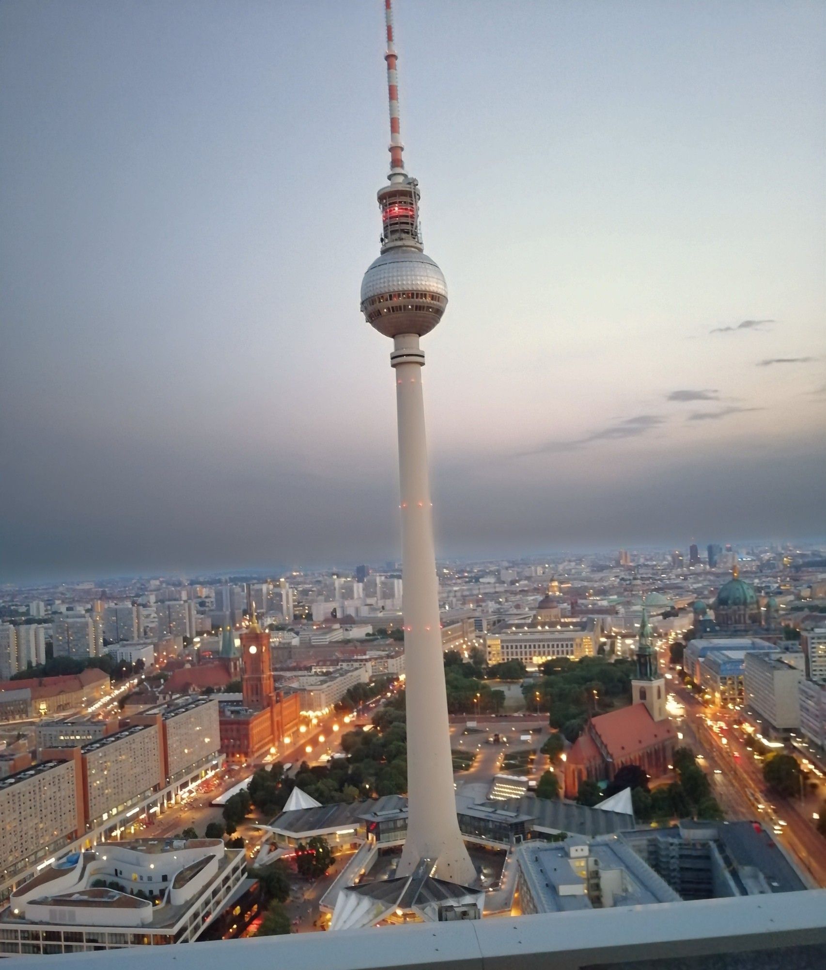 Blick auf den Fernsehturm von Berlin von einem Hochhaus (Terrasse des ParkInn) in der Dämmerung. Die Straßen sind gelb erleuchtet, im Hintergrund verschwimmen die Häuser im Dunst